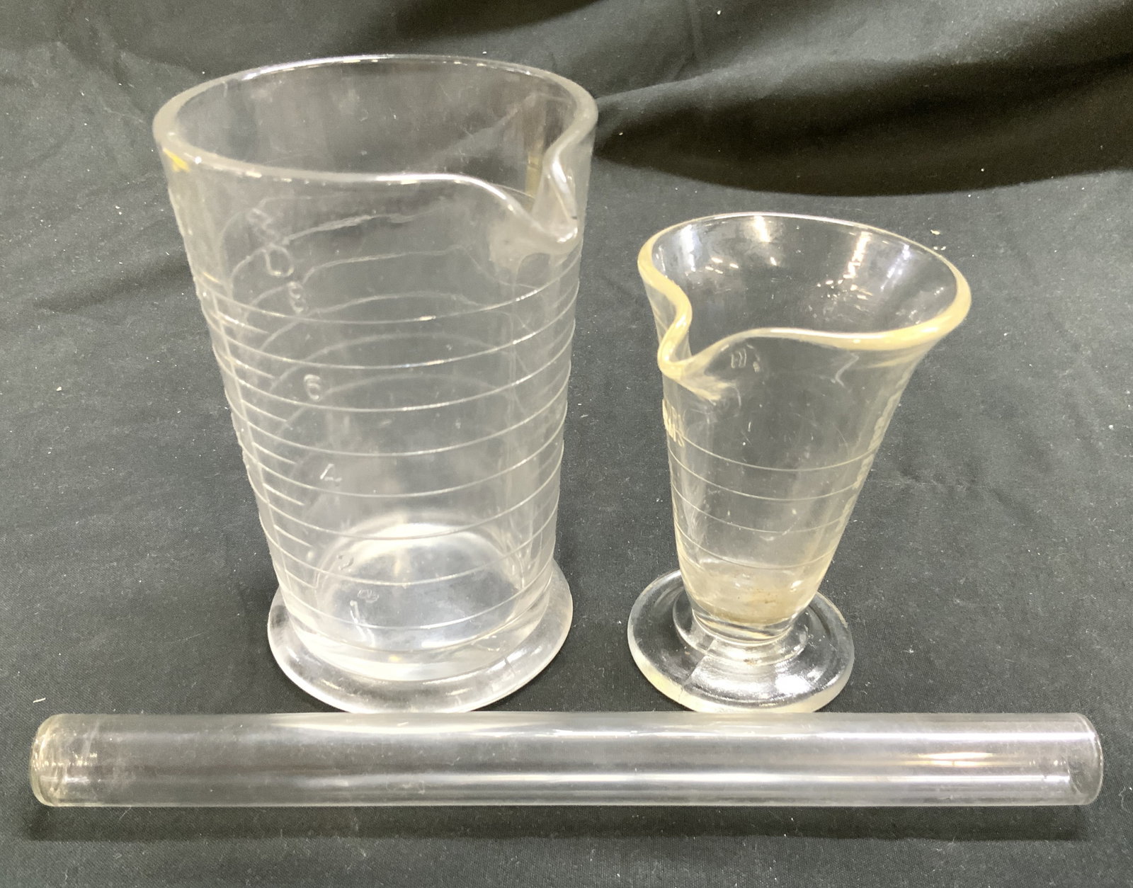 Lot 3 Glass Test Tube & Beakers: Lot includes 2 beakers and 1 test tube. Each piece in lot is glass. Lot includes one 1 Oz beaker & one 8 Oz beaker. Test tube measures approximately 8 inches tall. Larger beaker measures approximately