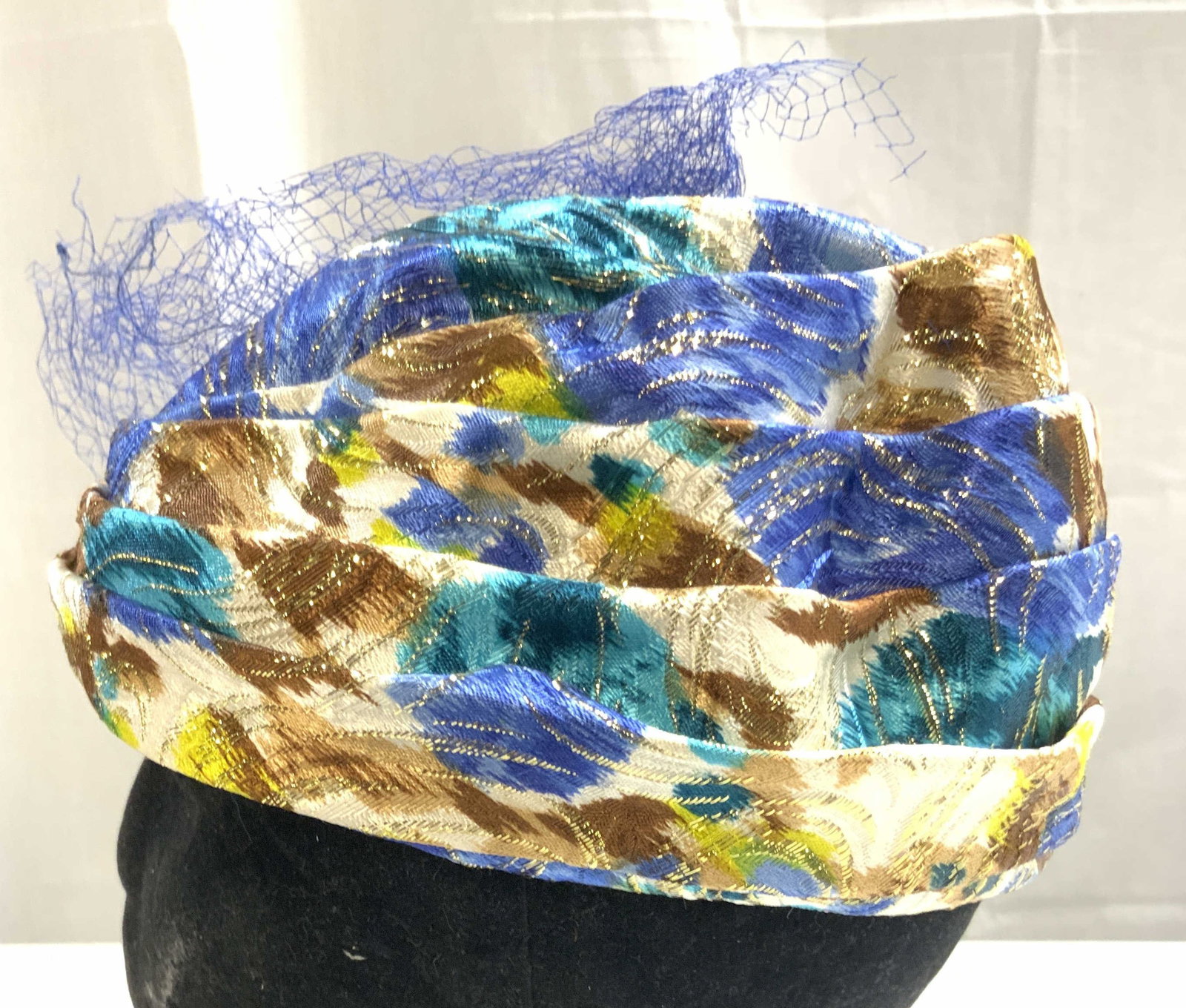 Vntg 1950s Womens Pillbox Hat W Netting: Pillbox hat is vintage circa 1950s. Piece has blue toned netting. Hat has intricate multi toned detail with gilt threaded areas. Interior has UNION MADE Tag. Hat measures approximately 8 inches wide 4