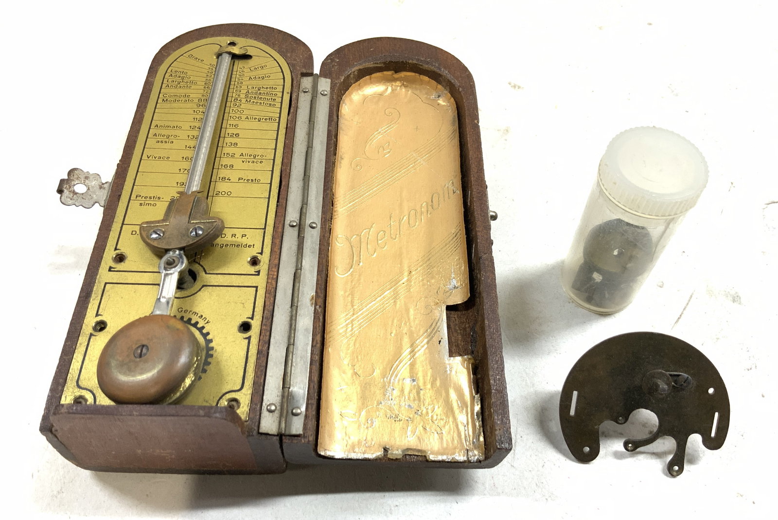 Antique German Coffin Style Metronome & Parts: Metronome is antique. Outer shell is brown toned and wooden. Interior is brass with black toned lettering. Reads MADE IN GERMANY. Lot also includes extra miscellaneous parts. Metronome has coffin form