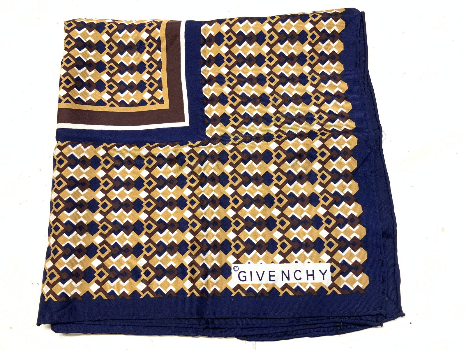 Vntg GIVENCHY Geometric Print Silk Scarf: Vntg GIVENCHY Geometric Print Silk Scarf Scarf appears to be possible silk & features a geometric pattern in shades of blue, gold & brown. Signed & marked. Reads, GIVENCHY. Surface wear consistent to