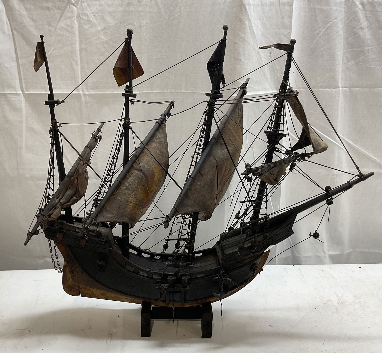 Atq Hand Crafted Wooden Model Ship w Stand: Antique hand crafted wooden model ship. Historical vessel with various symbol on sails, illegible due to residue and discoloration. Shoe shaped hull, wooden masts, and wooden toggles. Signs of age pre