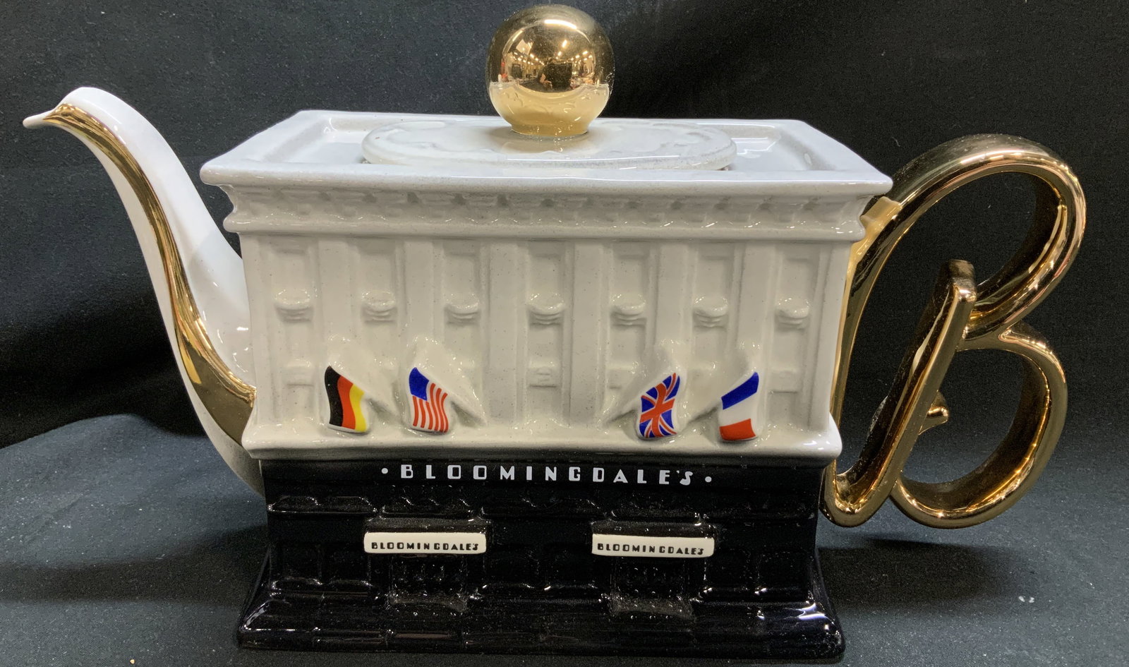 SIGNED Cardew Bloomingdales Porcelain Teapot ENG: SIGNED Cardew Bloomingdales Porcelain Teapot ENG Porcelain teapot featuring Bloomingdales department building, with international flags & a large B handle. Teapot is lidded & features a gold-toned kno