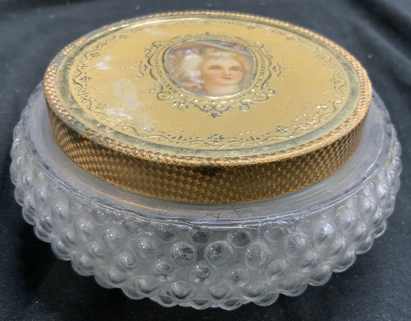 Vntg Hobnail Gls Powder Jar W Gilt Metal Lid: Powder jar is Vintage. Piece is glass with hobnail beveled detail. Piece has gilt metal lid with gilt metal lid. Center of lid has portrait of female figure. Powder jar measures approximately 5 inches