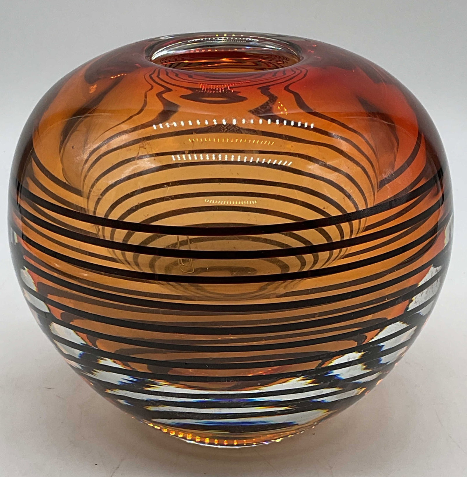 Hand Blown Orange Black Swirl Art Glass Vase: Hand blown art glass vase. Style of MURANO, no visible signature. Thick cased glass in orange to clear with black swirling band design. Measures approx 6.5 x 5.74 inches. Piece has weight. Some scratc