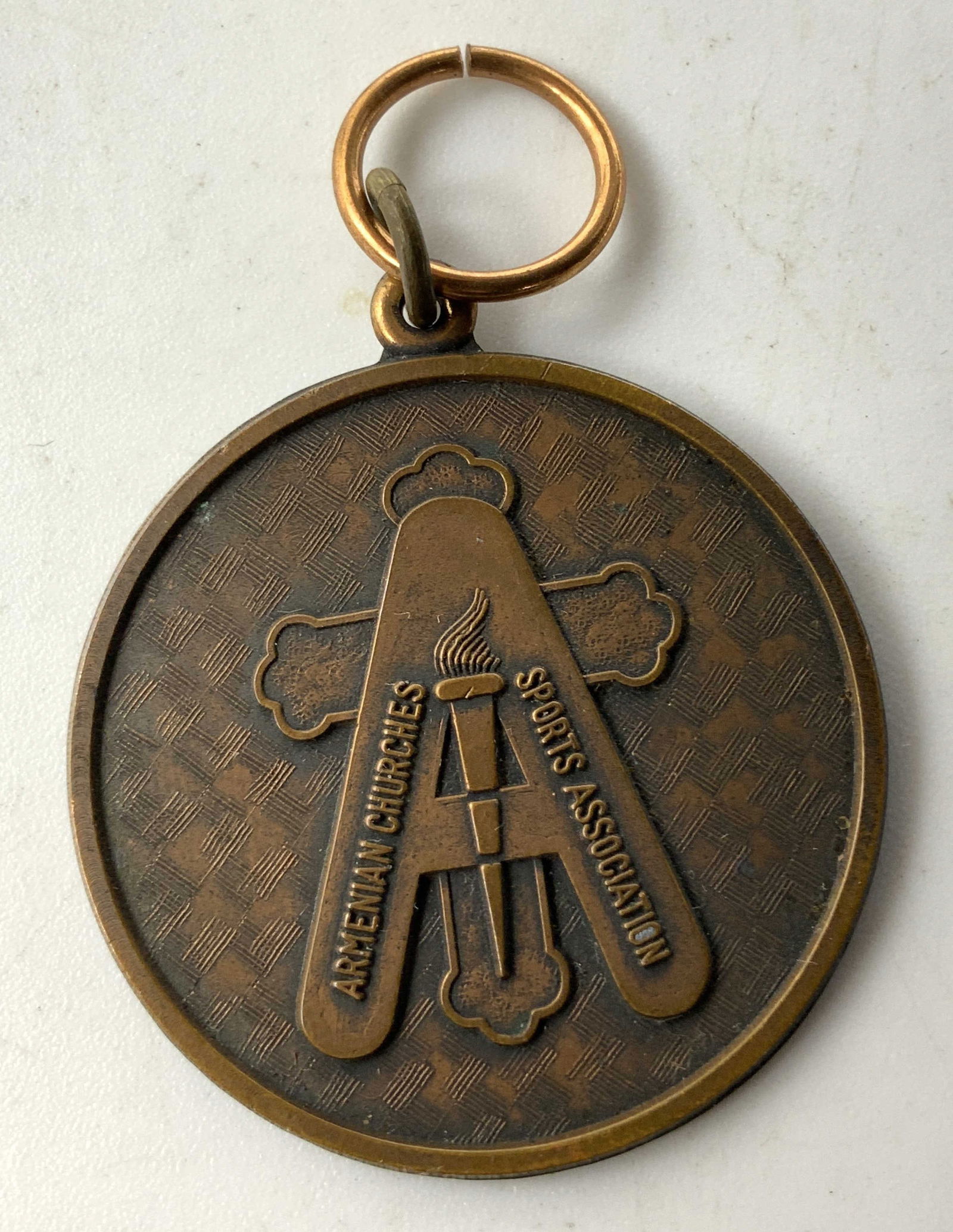 Copper Plated ARMENIAN CHURCHES SPORTS Assoc Medal: Medal features a cross & a torch & lettering that reads ARMENIAN CHURCHES SPORTS ASSOCIATION. Medal appears to be copper/copper plated. Signed & marked. Surface wear consistent to age, use & exposure.