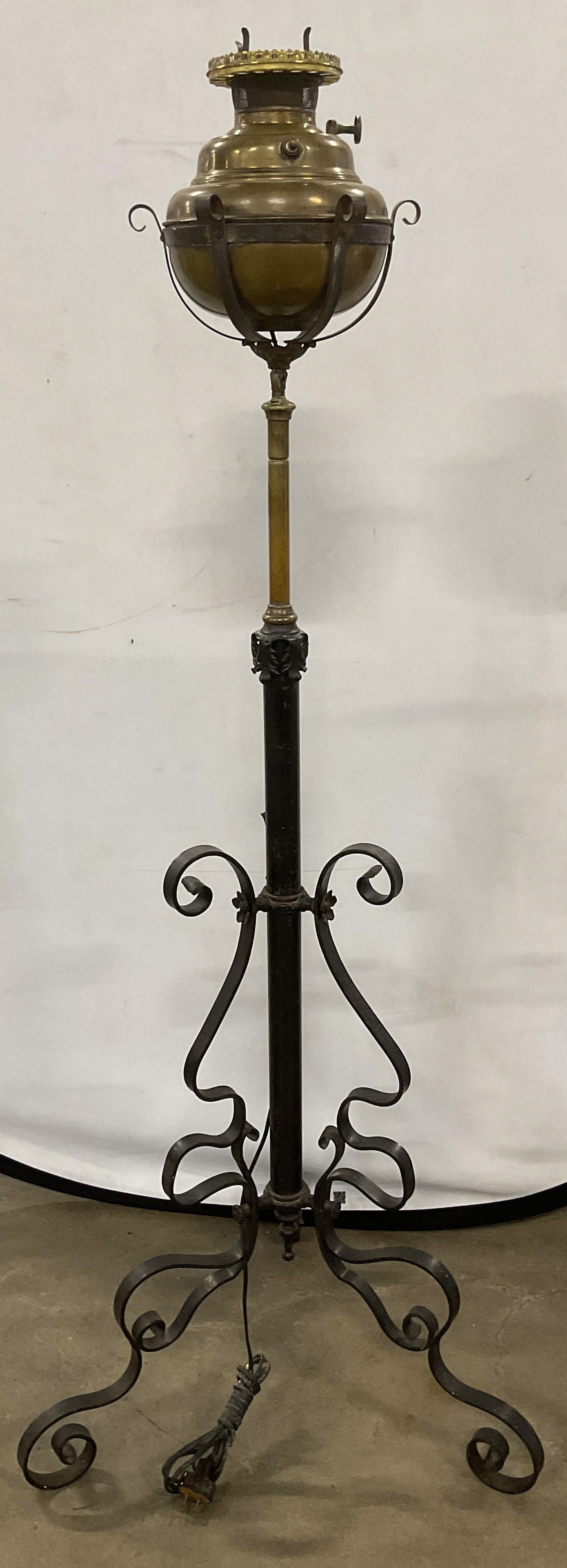 Antique Wrought Iron Brass Piano Oil Lamp: Antique piano floor lamp. Around iron base with Parker brass oil lamp bowl. Signed on brass. Curved tripod pedestal base. Electrified. Not tested. Piece is heavy. Measures approx 20.5 x 18 x 52 inches