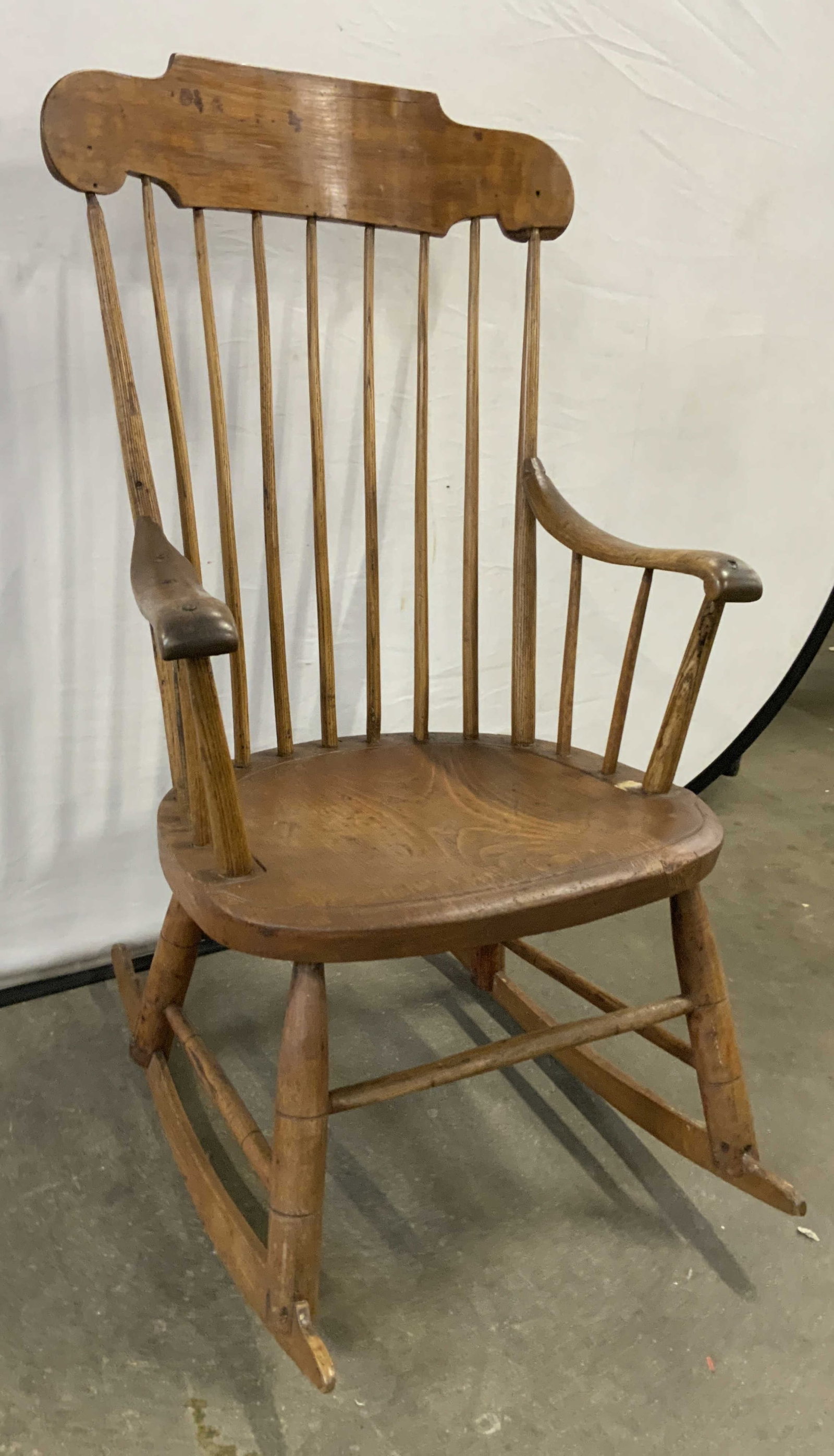 Vintage Wooden Spindle Back Rocking Chair: Rocking chair is vintage and wooden. Piece is beige toned. Chair has spindle backrest. Supports have stretchers in between. Chair has armrests. Piece measures approximately 40 inches tall 22 inches wi