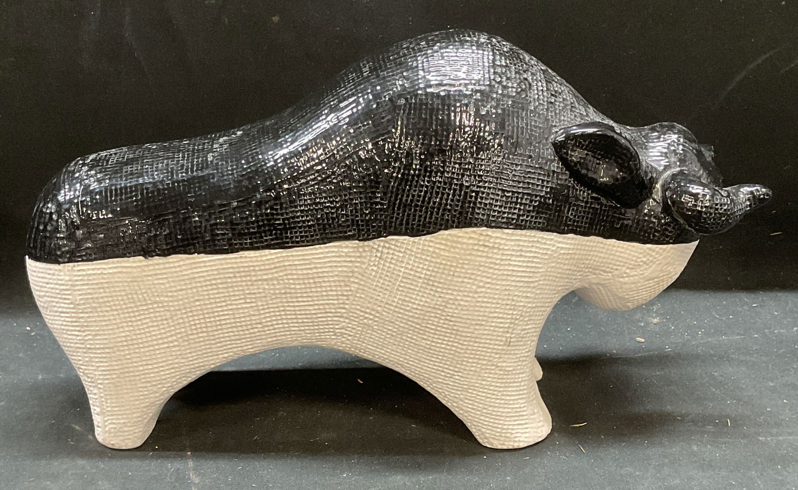 Textured Black & White Ceramic Bull Figural: Textured white ceramic bull figural with hand painted black glaze. Measures approx 10.75 x 3.75 x 6 inches. Some surface wear consistent with exposure. Bull figural, ceramic bull, decorative arts, hom