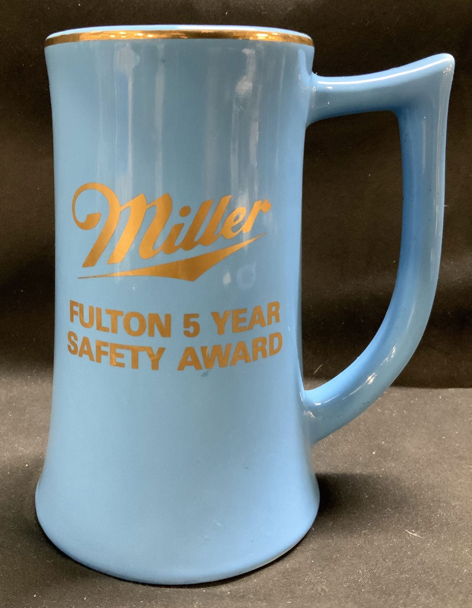 Vntg Miller Fulton 5 Year Safety Award Mug USA: Light blue mug features the Miller logo in gold, along with Fulton 5 Year Safety Award. Signed & marked on underside. Reads, USA. Mug is ceramic material. Surface wear consistent to age, use & exposur