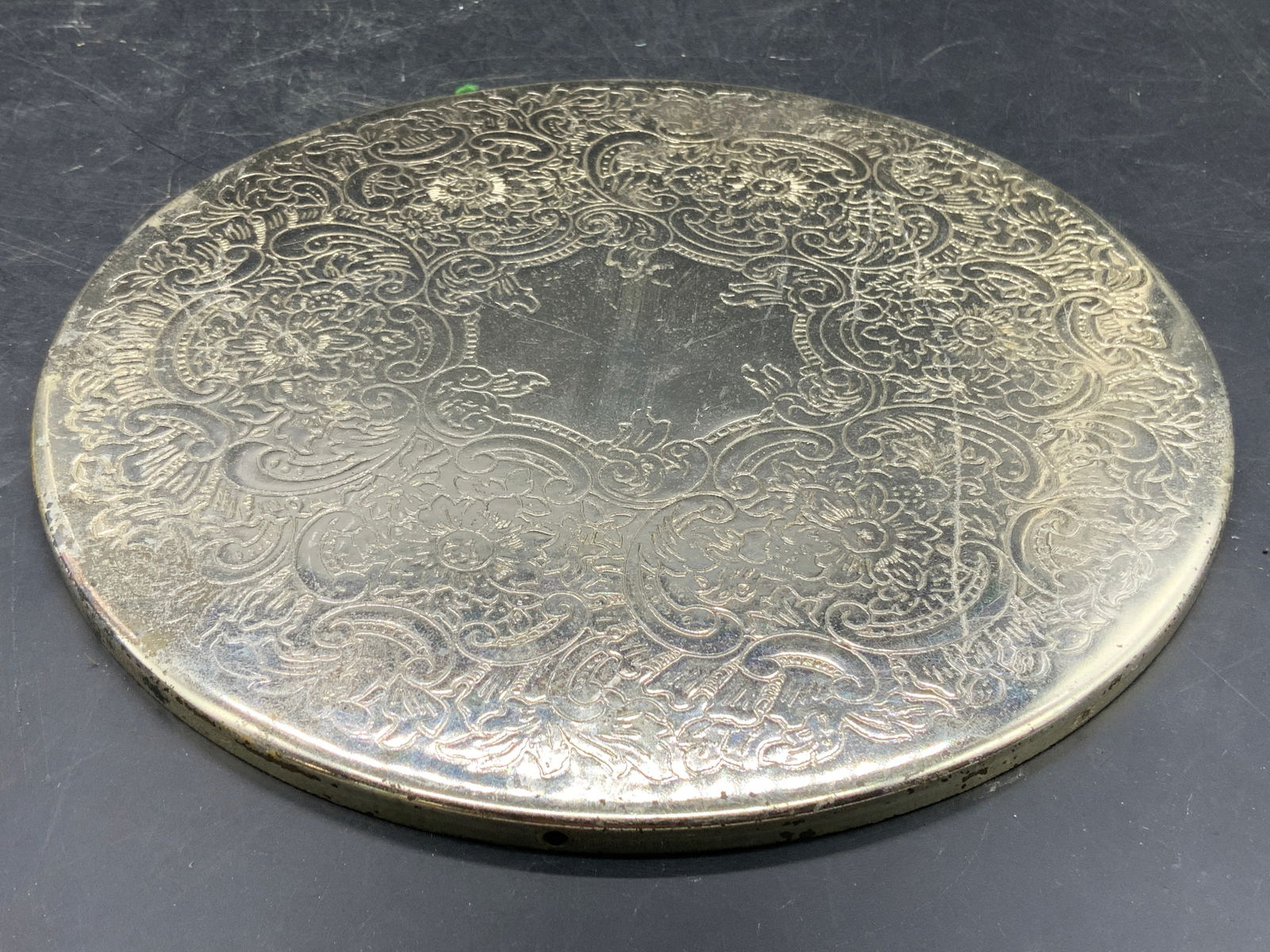 Silver Plate Ornate Circular Etched Wall Hanging: Wall hanging is vintage. Piece is silver plated. Piece has etched ornate floral, leaf & scroll relief detail. Wall hanging has circular form. Piece measures approximately 8.75 inches diameter. Wall ha