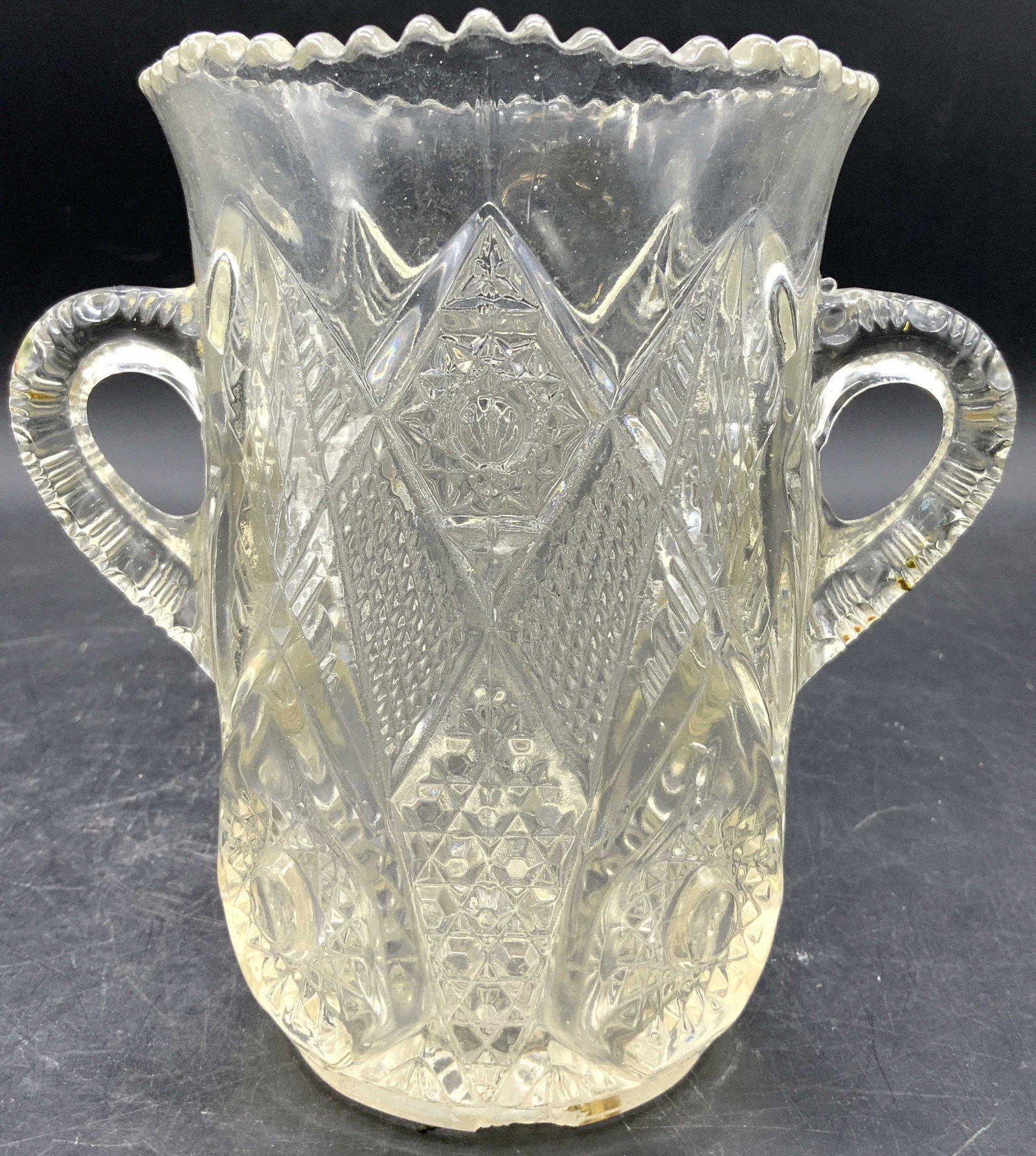 Antique US Glass Hobstar Celery Vase w Handles: Appears to be by US GLASS (No apparent markings). Celery vase appears to be antique possibly vintage. Piece has intricate geometric relief detail. Vessel has saw tooth rim. Sides of vase have handles.