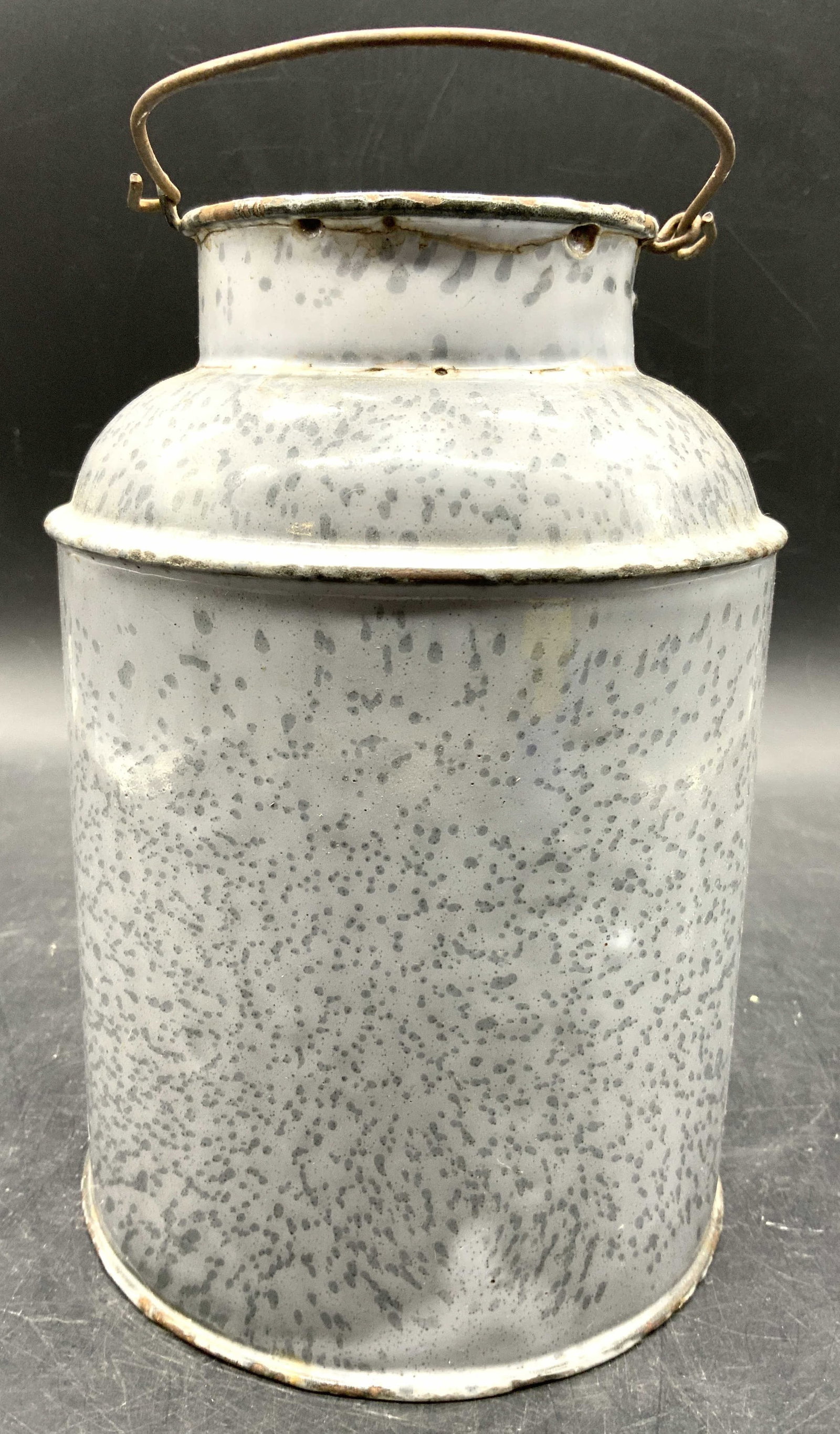 Vtg Graniteware Enamel Milk Can W Handle: Milk can is vintage. Piece is graniteware enamel. Slate toned with speckled detail. Milk has arch form metal handle. Piece has circular form base and mouth. Outer rim has lip. Piece measures approxima