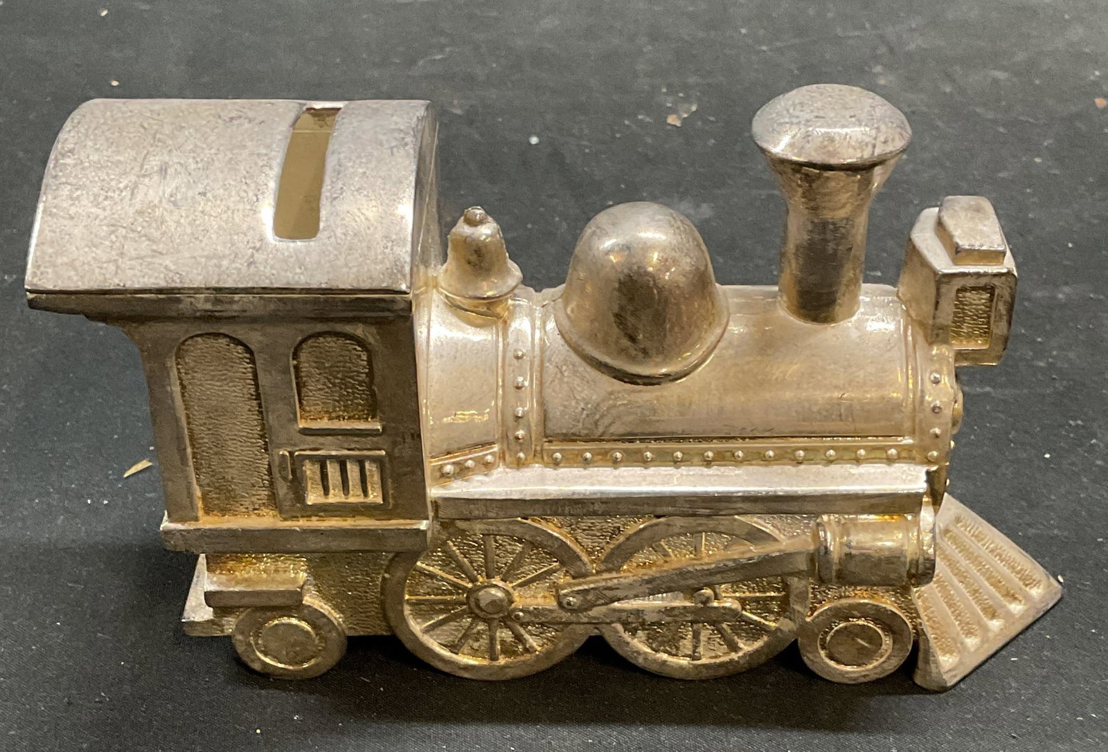 Vintage Silver Tone Train Coin Bank: Vintage silver tone train motif coin bank. Cast metal. Measures approx 6 x 2 x 3 inches. Some patina and scratching, cover to underside needs replacement. Train, silver tone train, coin bank, metal co