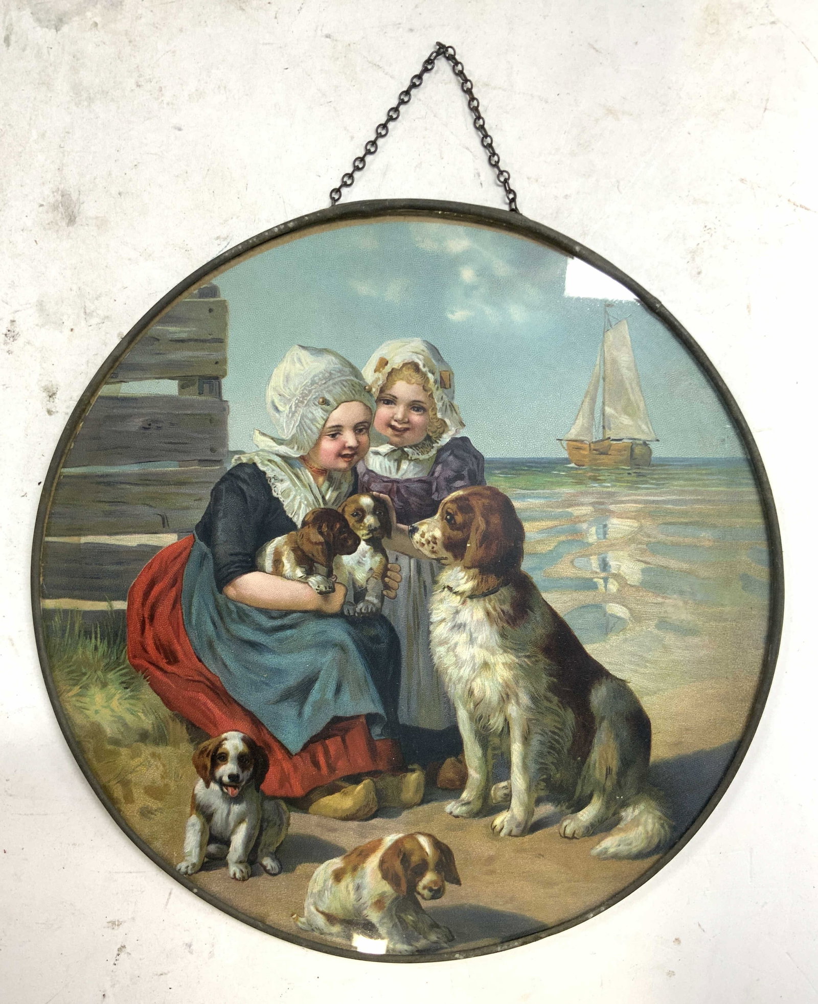 LITTLE HOLLANDERS Print Kids & Dogs BELGIUM: Backside of piece is marked made in BELGIUM. LITTLE HOLLANDERS Print depicting Dutch children and dogs near the shoreline with a boat in the background. Print is inside a metal circular frame with gla