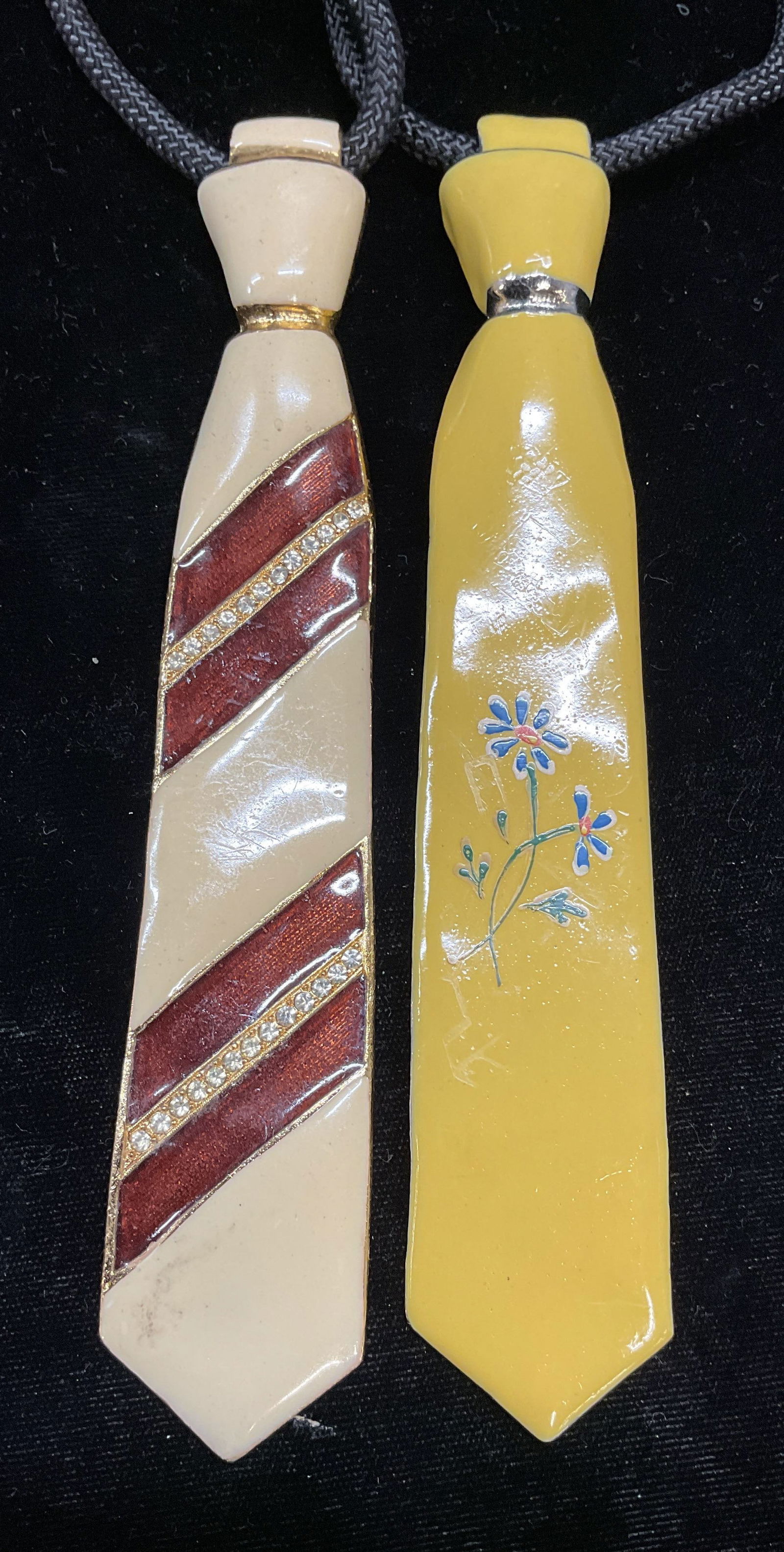 Lot 2 Signed Enamel Tie Pendant Necklaces 6.75in: Lot of 2 pieces. Tie motif pendants. Gold and silver tone enameled metal in yellow and red. One with floral design. One piece signed illegibly. Black cord necklaces. Pendants measure approx 6.75 x 1.2