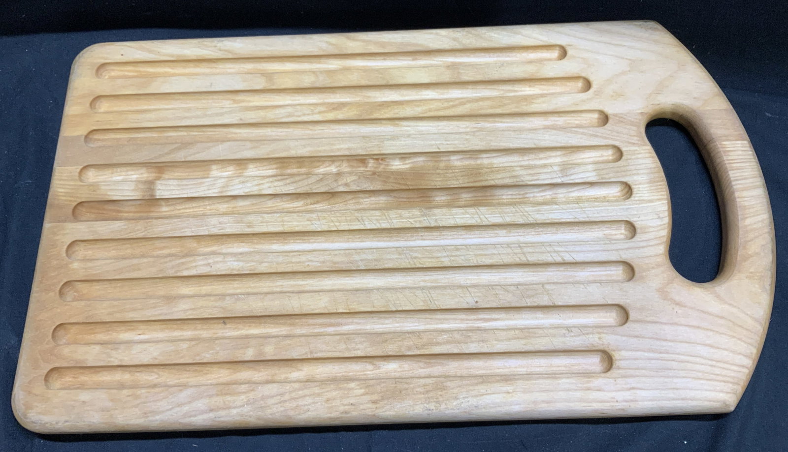 John McLeod Design Wooden Bread Cutting Board: Bread cutting board is wooden material & features several parallel grooves used to catch crumbs when slicing bread. Signed & marked on underside. Reads, A JOHN MCLEOD DESIGN & printed signature. Surfa
