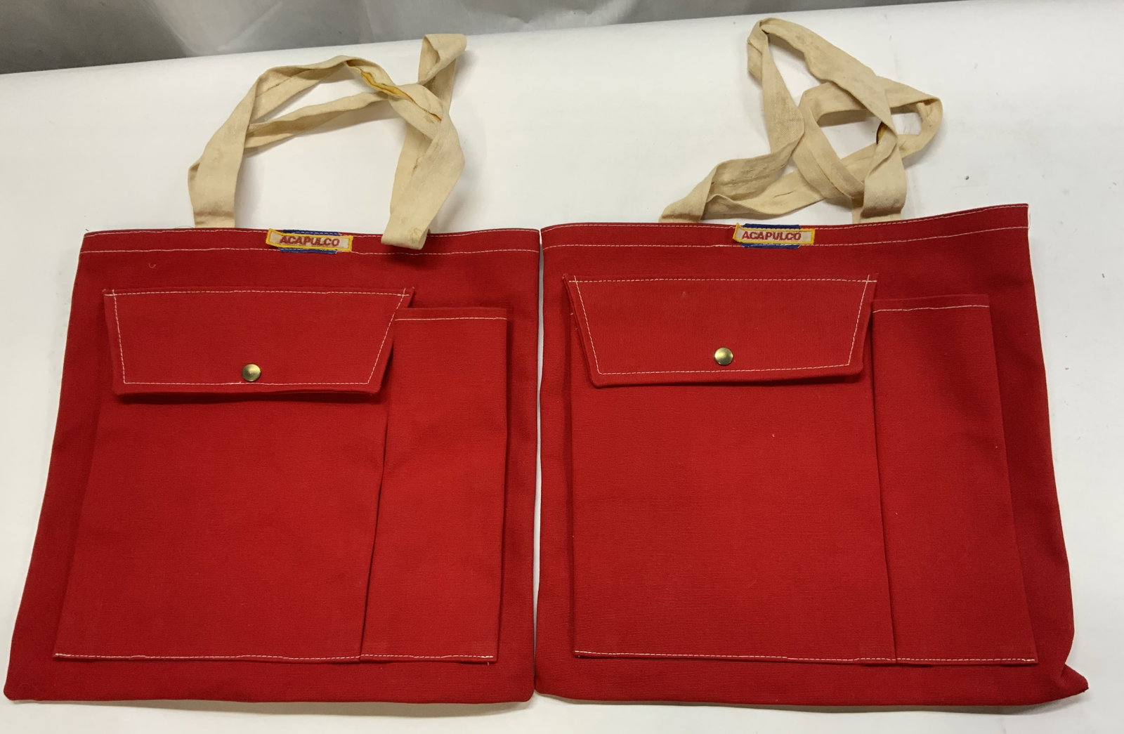 2 ACAPULCO Red Canvas Tote Bags: 2 ACAPULCO Red Canvas Tote Bags Bags appears to have a canvas material & has ACAPULCO sewn onto the top part of the bag. Bag is dark red with a pocket in the front. Surface wear consistent to age, use