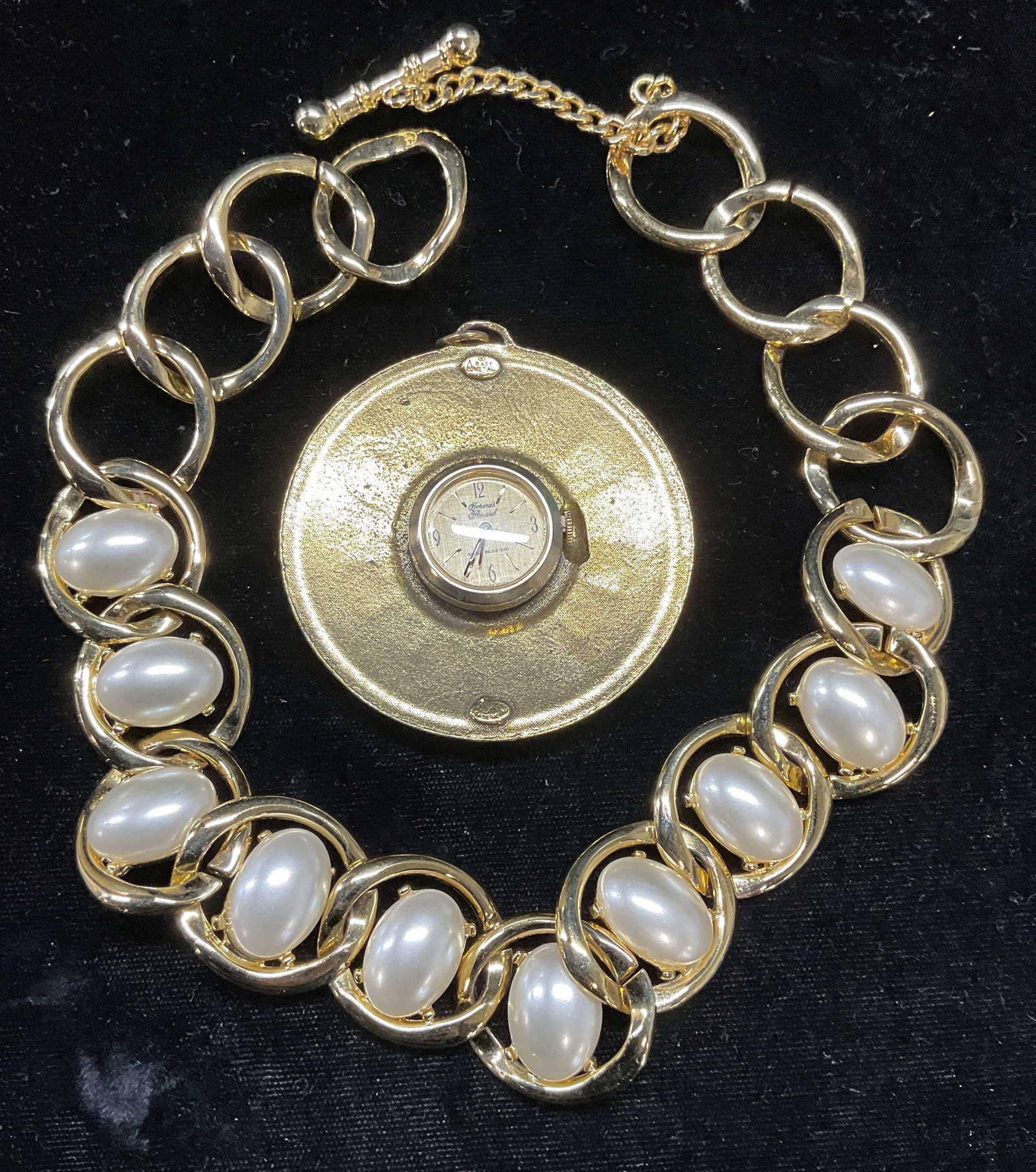 Lot 2 Gervais Perard Watch Pendant, Faux Pearl +: Lot of 2 pieces. Gervais Perard gold tone watch pendant with crest motif. Signed. Not tested. Measures approx 2.5 inches wide. Gold tone faux pearl necklace. Drop length approx 7 inches. Some wear inc