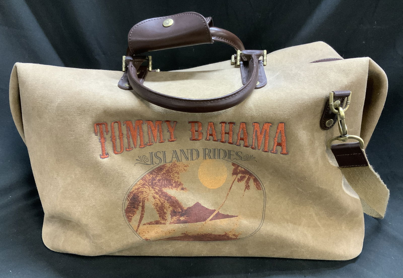 Vntg Tommy Bahama Island Rides Duffel Bag W Strap: Duffle bag features a tan canvas material and features a graphic on the front. The graphic includes the TOMMY BAHAMA ISLAND RIDES logo in a distressed, reddish-orange font, set above a tropical scene