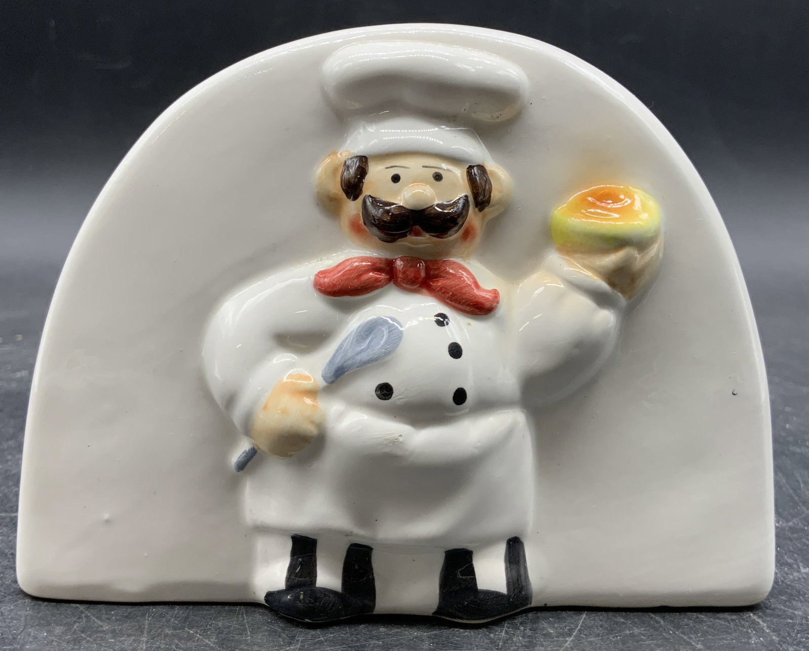 Vintage Porcelain Bistro Chef Napkin Holder: Napkin holder is vintage. Piece is white toned and porcelain with hand painted detail depicting a portly bistro chef. Napkin holder measures approximately 3.5 inches tall 4.5 inches wide 2.5 inches de