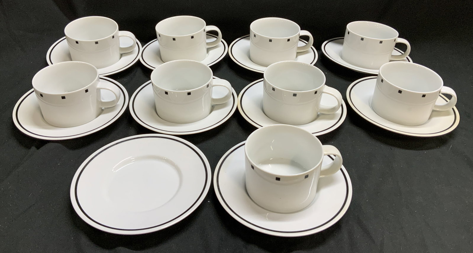 Lot 19 Sasaki Metropolis 1986 Teacups&Saucers JAP: Lot includes, 9 teacups & 10 saucers. Pieces are fine china material & cups feature a distinctive black square pattern & black trim design. Signed & marked on underside. Reads, SASAKI. FINE CHINA. MET