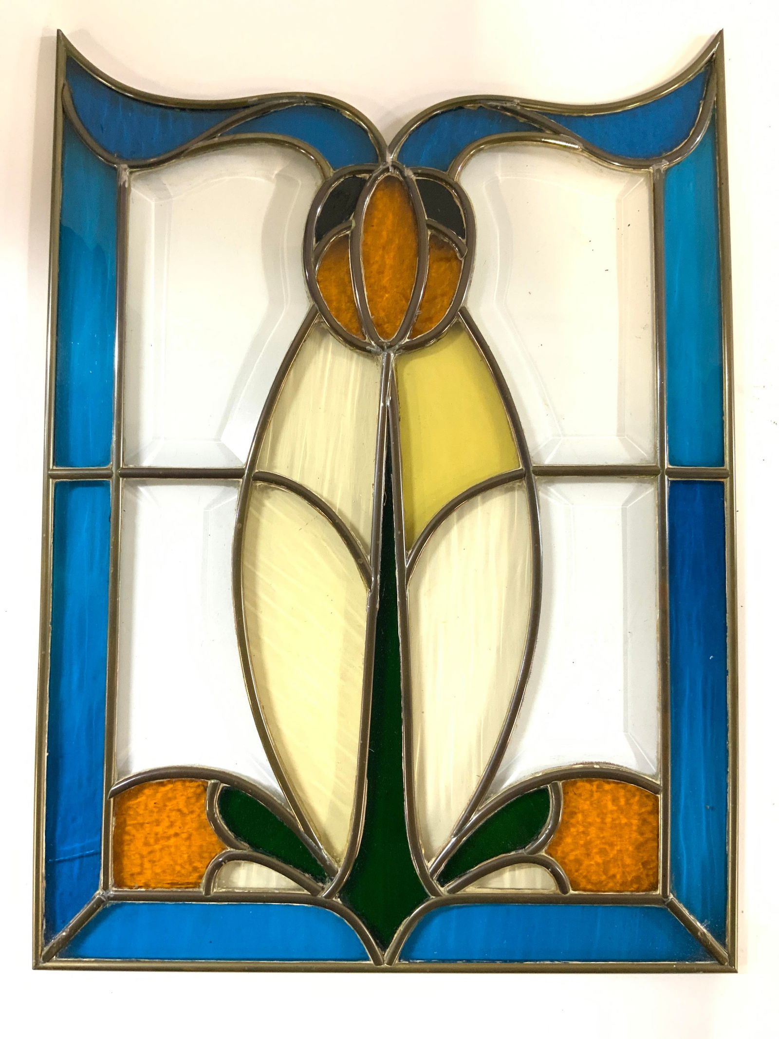 Floral Stained Glass Art Glass Wall Hanging 18in: Wall hanging is stained glass piece has floral detail. Clear glass areas are beveled. Piece has blue toned edges. Center of piece has green, orange, yellow and black tones. Stained glass wall hanging