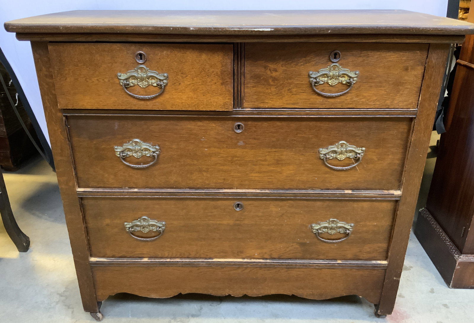 Antq 4 Drawer Wooden Dresser On Casters: Dresser is antique. Piece is brown toned and wooden, dresser has 4 drawers each with gilt metal handles and hand dovetailing. Top 2 drawers have keyholes. Base of dresser has casters. Measures approxi