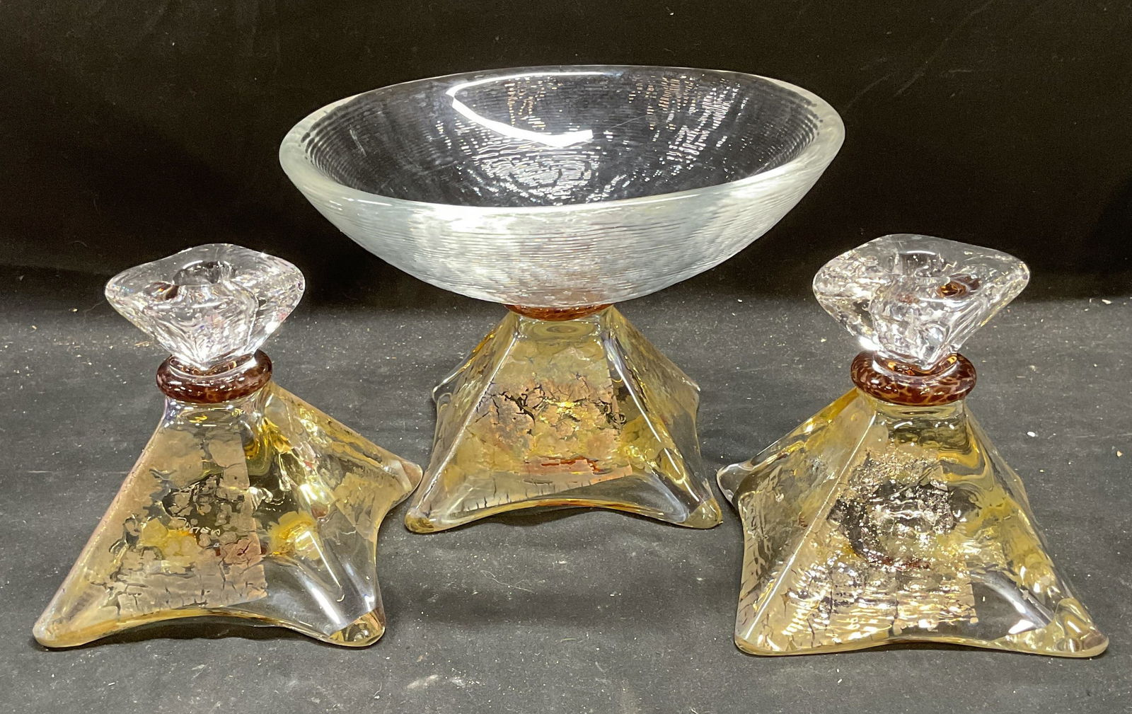 3 Wilsea OBrien Art Glass Bowl & Candlesticks: Lot of 3 pieces. Wilsea OBrien hand blown art glass garniture set. Includes pedestal bowl and pair of candle holders. Wide square bases tapering up to bowl and candle sockets. Geometric circular, tria