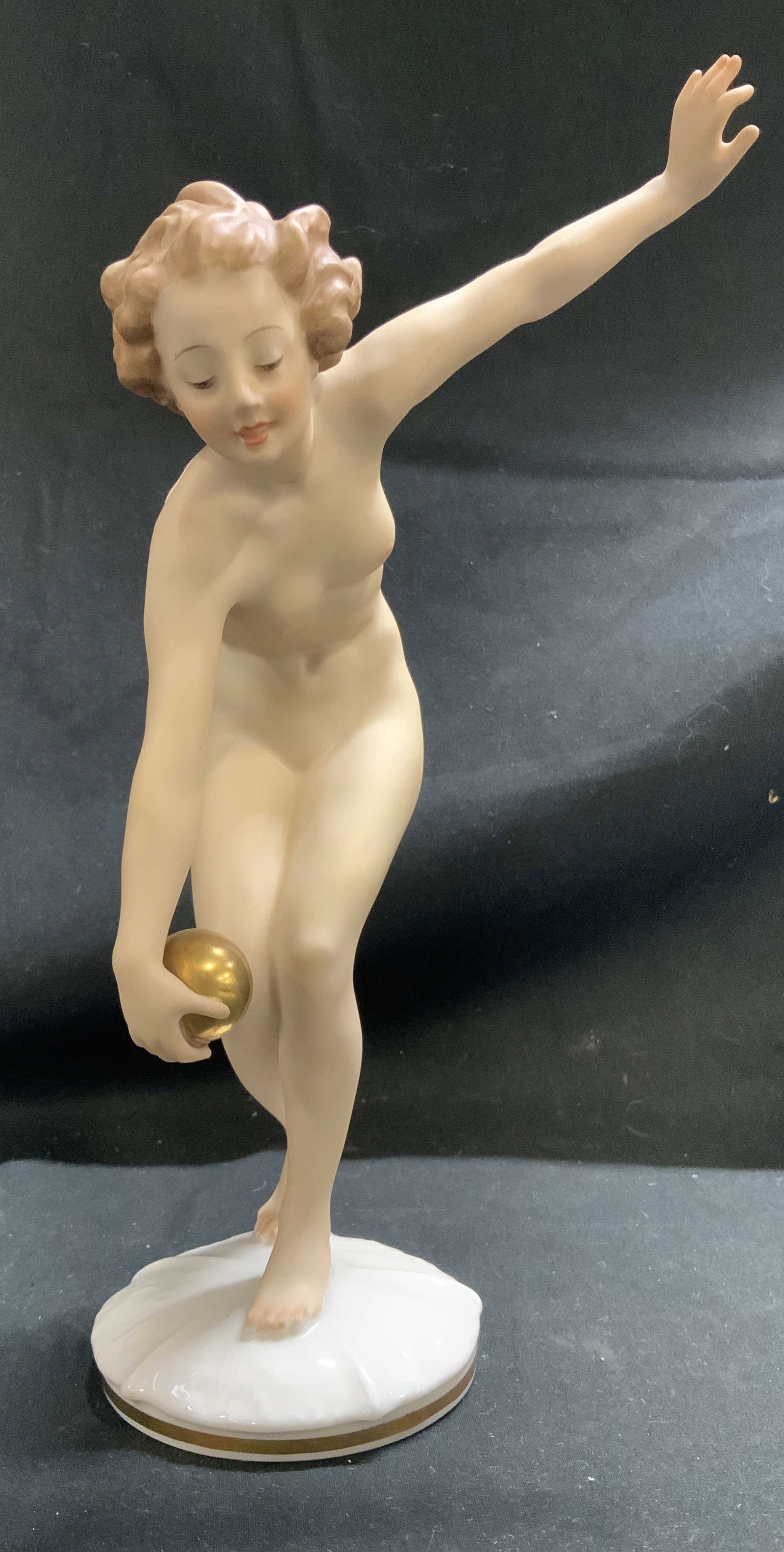 Vtg Hutschenreuther Ball Player Porc Fig. GERMANY: Porcelain figurine known as The Ball Player, designed by Karl Tutter. The figurine depicts a nude woman holding a golden ball. Fig is standing on white round base w gold accents. Surface wear consiste