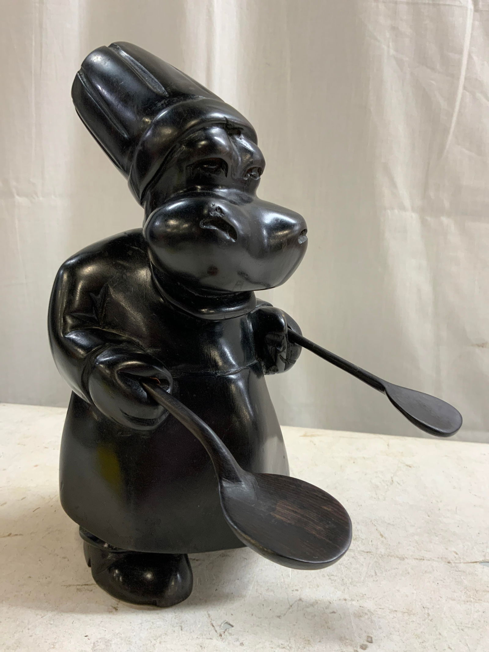Lacquered Chef Hippo Cooking Companion: Hippo figure is lacquered, possibly wooden possibly composite. Piece is black toned. Depicts a chef Hippopotamus figure with spoons. Piece measures approximately 10 inches tall 5 inches wide 7 inches