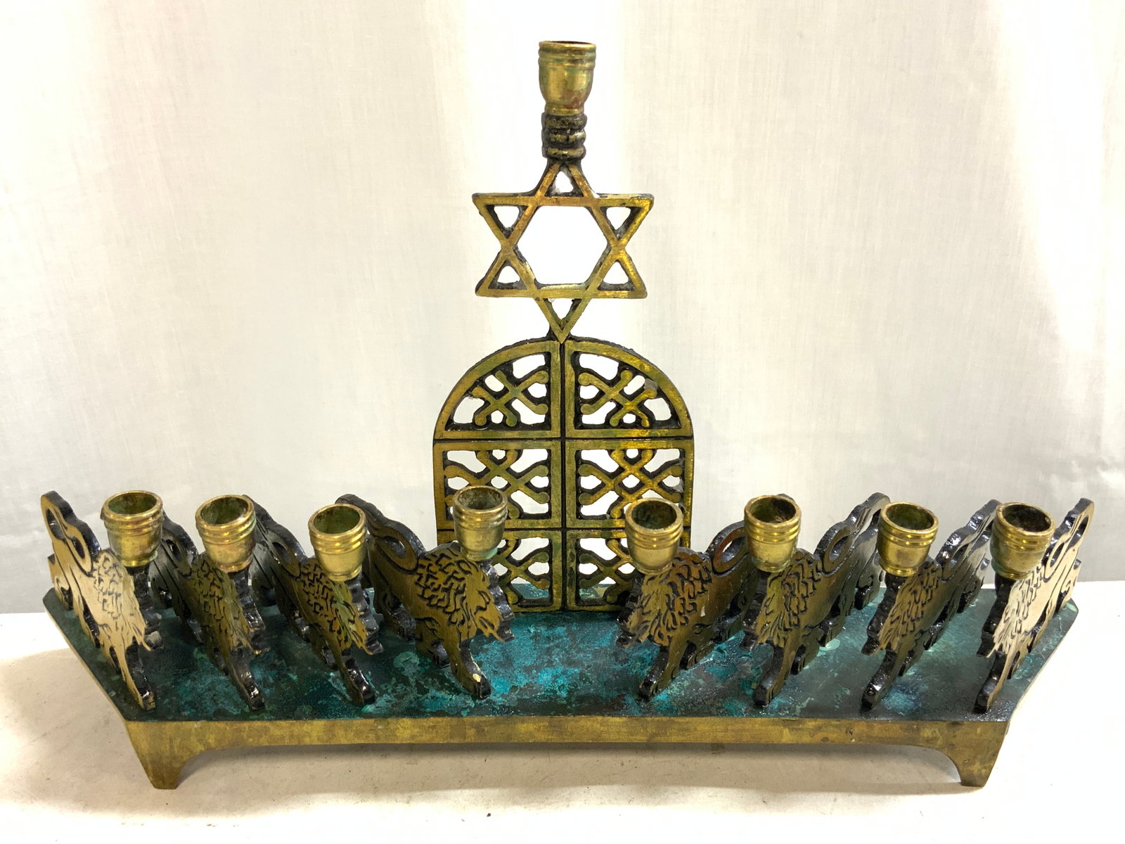 Vtg Brass Chanukah Menorah W Lion Motifs: Underside reads MADE IN ISRAEL. Menorah is vintage. Piece is gold toned, appears to be brass. Center of piece has tombstone form and Star of David. Menorah has lion motifs with 8 lion figures. Measure