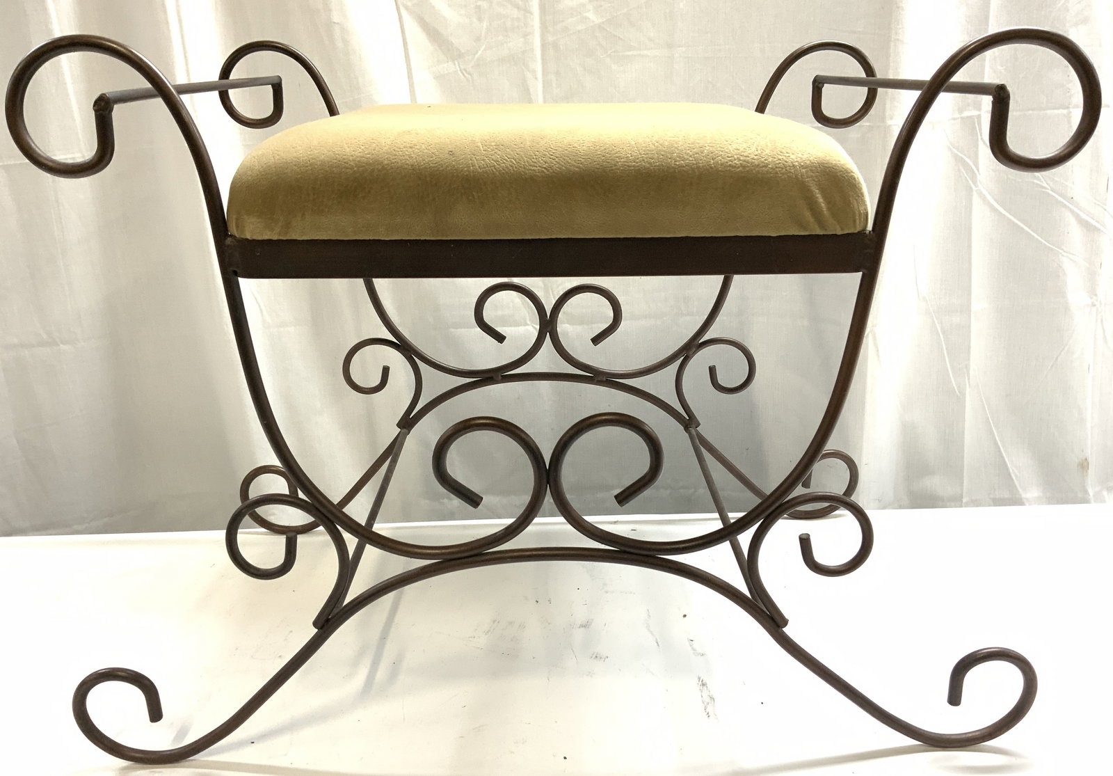 DOMISTYLE INC Upholstered Metal Bench: Tag on underside reads DOMISTYLE INC. Bench has tan toned upholstered seat, possibly textured suede possibly velvet. Piece has 4 curled feet. Bench has handles at sides. Piece measures approximately 2