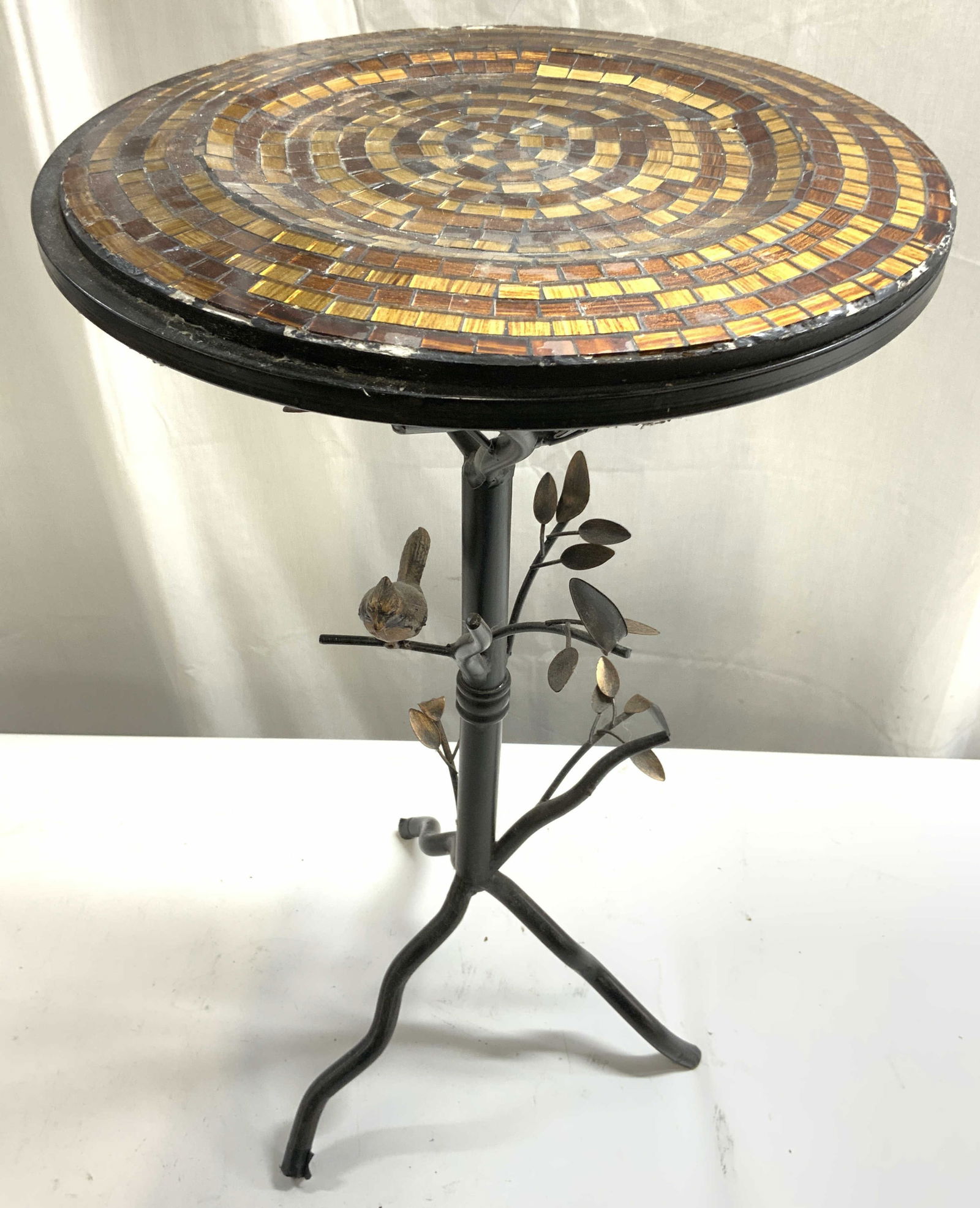 Pier 1 Perched Bird Brnzd Accent Tbl Gls Top: Table appears to be PIER 1 (No apparent markings). Table has circular form top with brown and amber toned glass mosaic detail. Base appears to be bronzed possibly iron. Piece has bird perched on branc