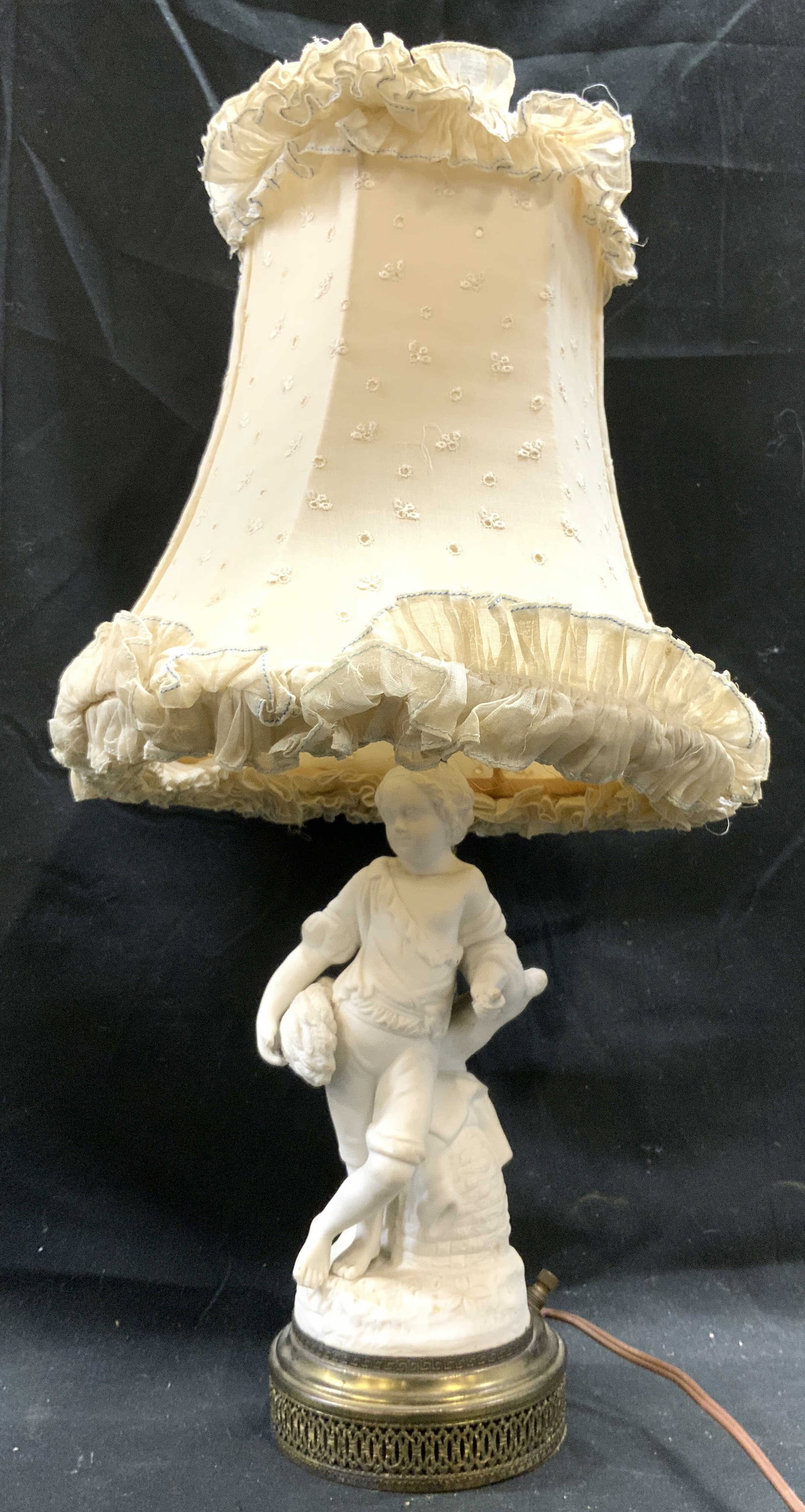 Vtg Porcelain Boy Figure Lamp W Frilled Shade: Lamp has white toned porcelain male child figure. Piece has brass circular form base with pierced detail. Lamp base has twist switch. Lamp shed is cream toned with embroidered pattern detail and frill