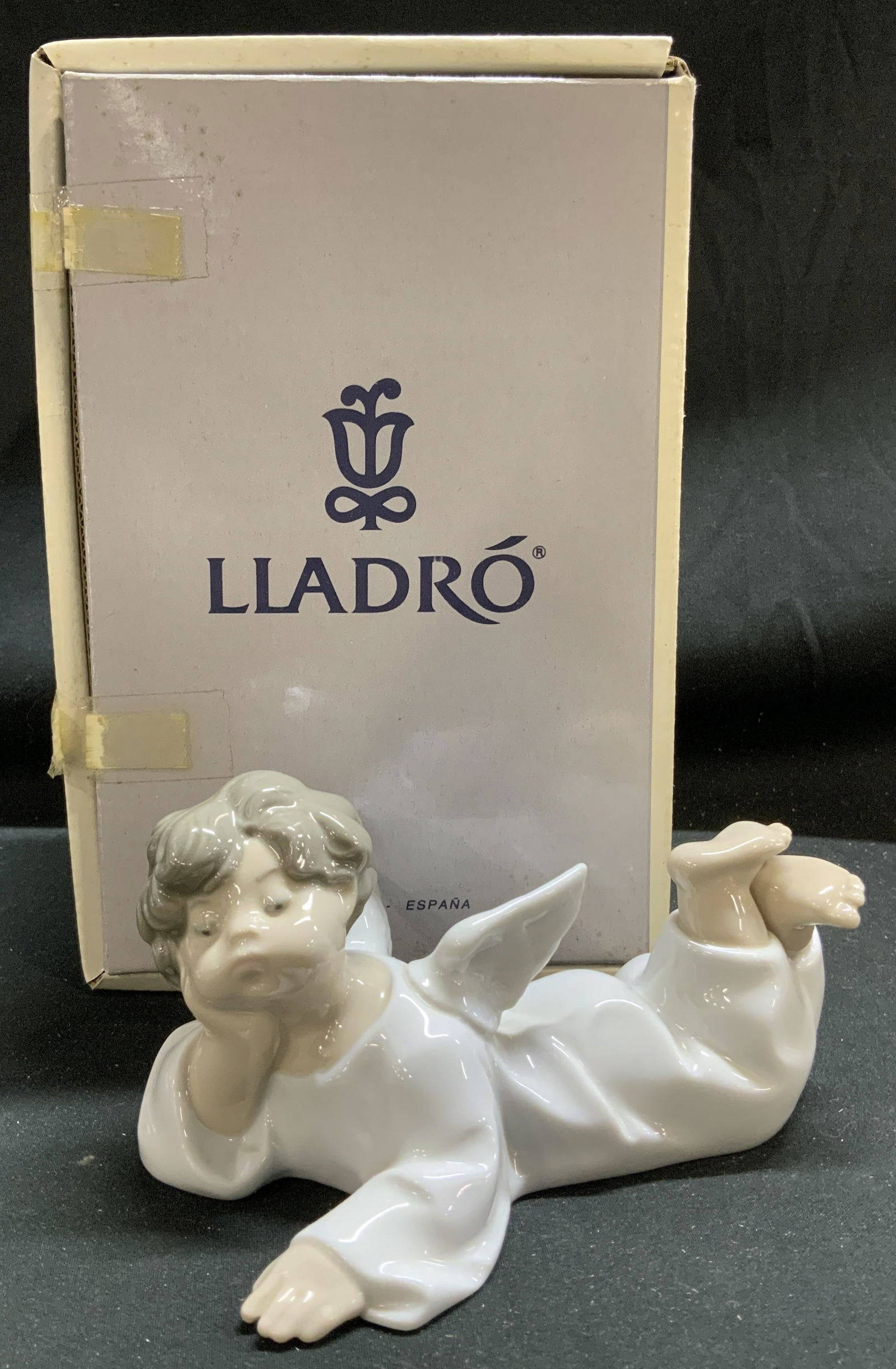 LLADRO Angel Laying Down Porc Fig. W Box SPAIN: Figurine is porcelain material & depicts an angel laying down. Angel is lying on its stomach with its head resting on its hands. Features a glossy white finish. Comes with original box. Surface wear c