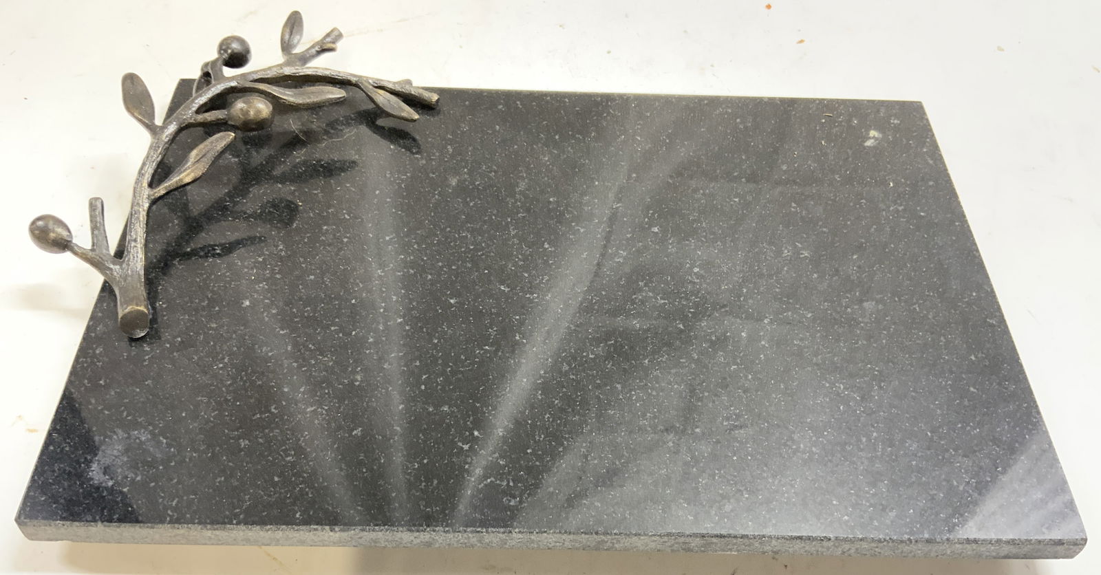 MICHAEL ARAM Sgnd Blk Granite Olive Branch Chsbrd: Underside has inscription signature which reads ARAM. Piece is black toned and granite. One side had metal olive branch handle. Underside is footed. Piece measures approximately 12 inches long 8.75 in