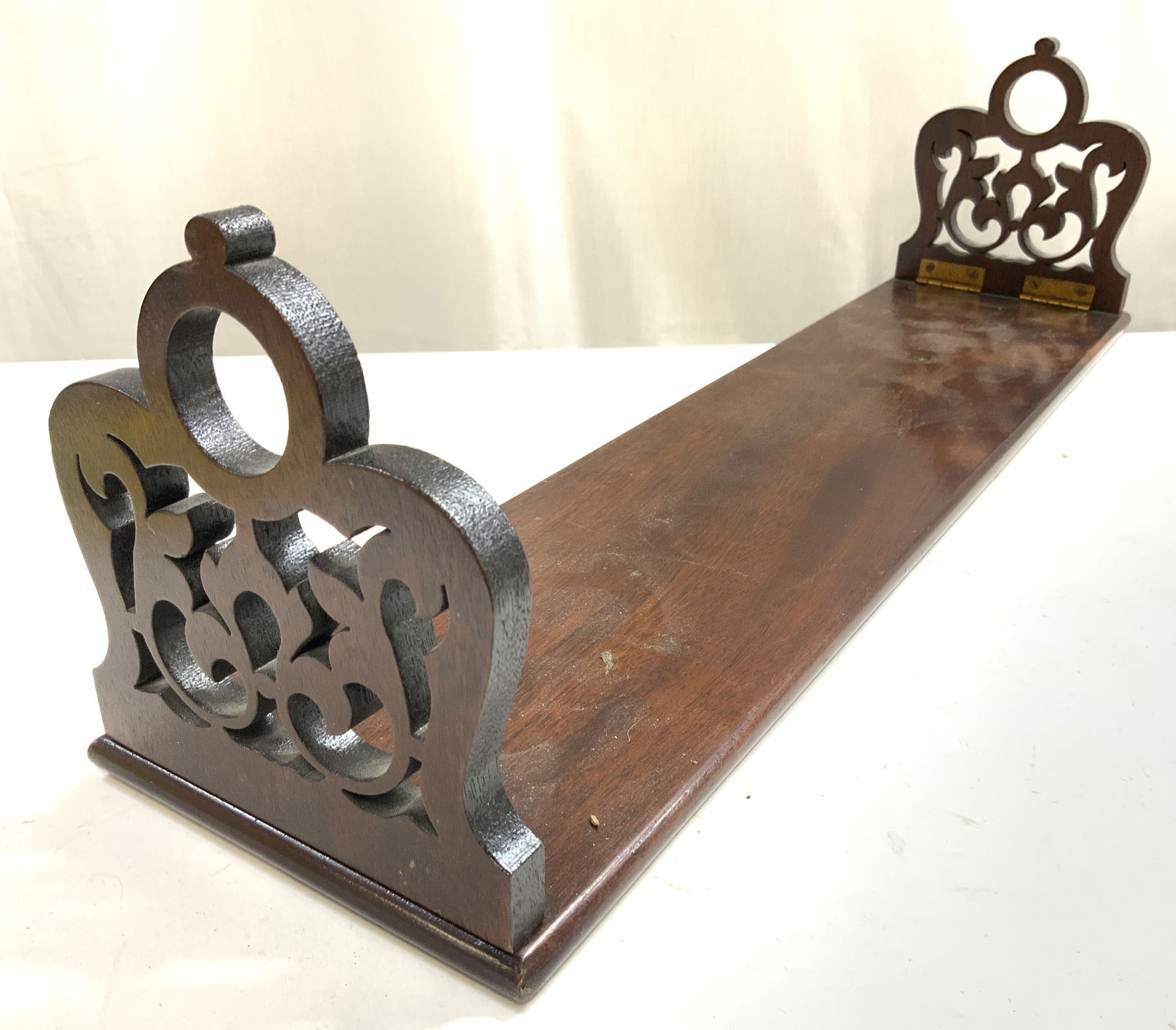 Vintage Carved Wooden Folding Bookend: Bookend is vintage and wooden. Piece is brown toned, possibly mahogany. Ends of piece fold, each have copper toned metal hinges. Each end has carved curled and pierced detail. Bookend measures approxi