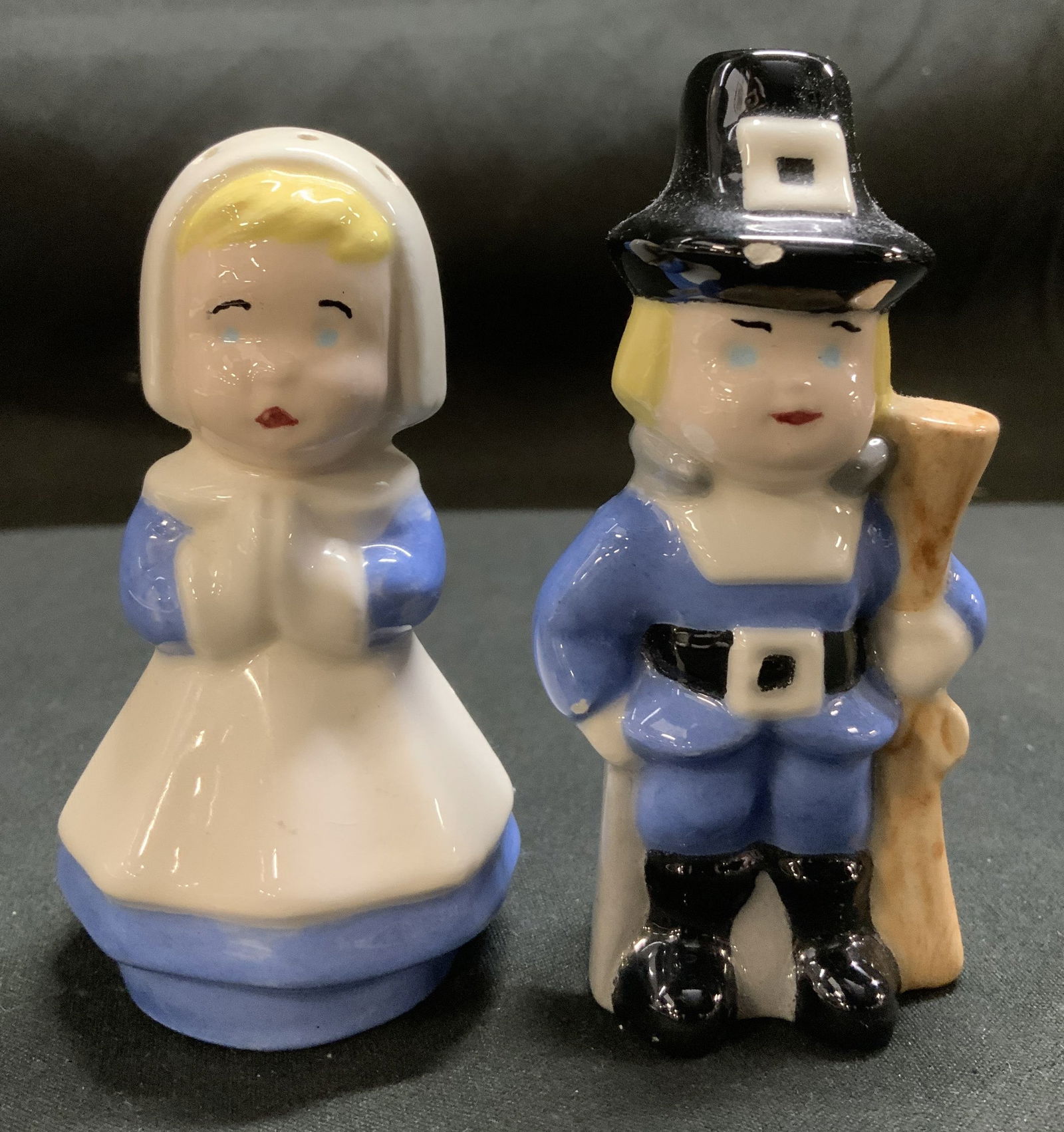 Vntg Signed Pilgrim Couple Salt & Pepper Shakers: Salt & pepper shakers are ceramic material & depict a pilgrim couple. Male figure is wearing a black hat & holding a rifle, and female has a white bonnet and blue dress. Signed & marked on underside.