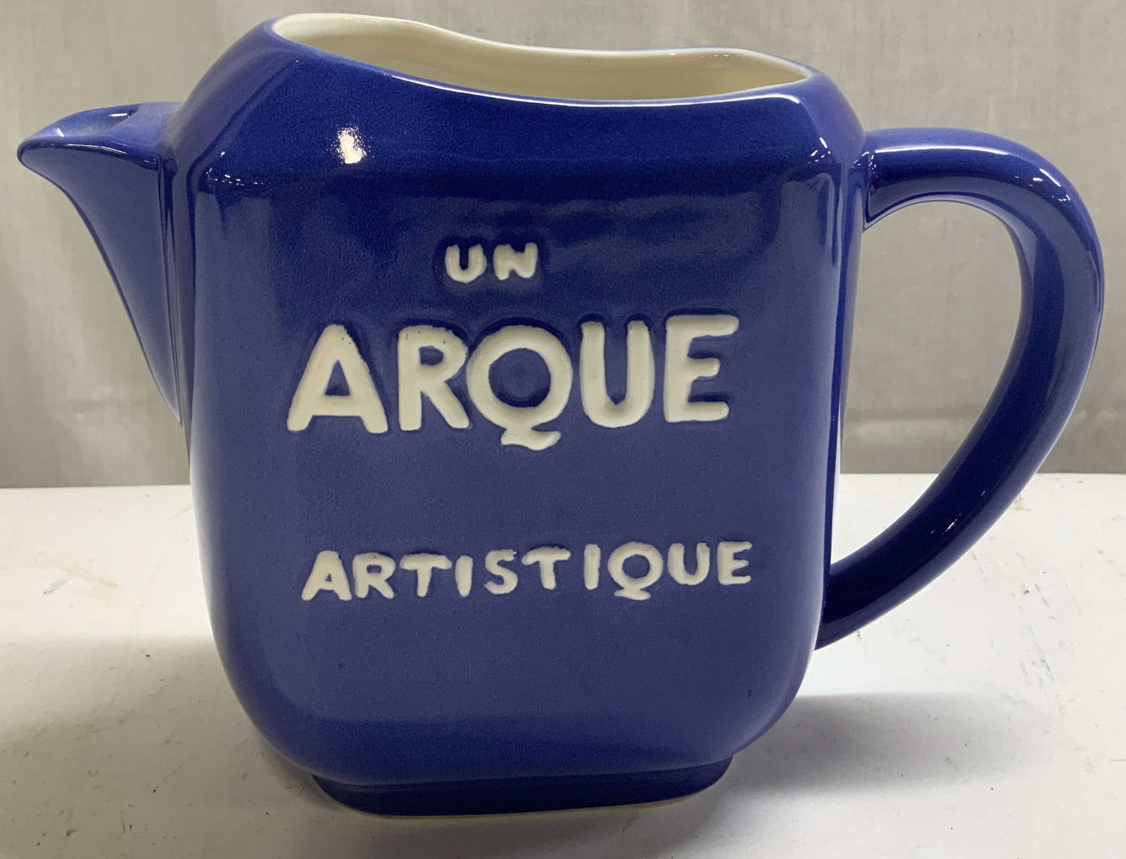 Restoration Hardware Un Arque Artistique Pitcher: Pitcher is ceramic material & depicts a vintage-style. Dark blue pitcher with raised white lettering. Reads, UN ARQUE ARTISTIQUE. Glossy finish. Signed & marked on underside. Reads, RESTORATION HARDWA