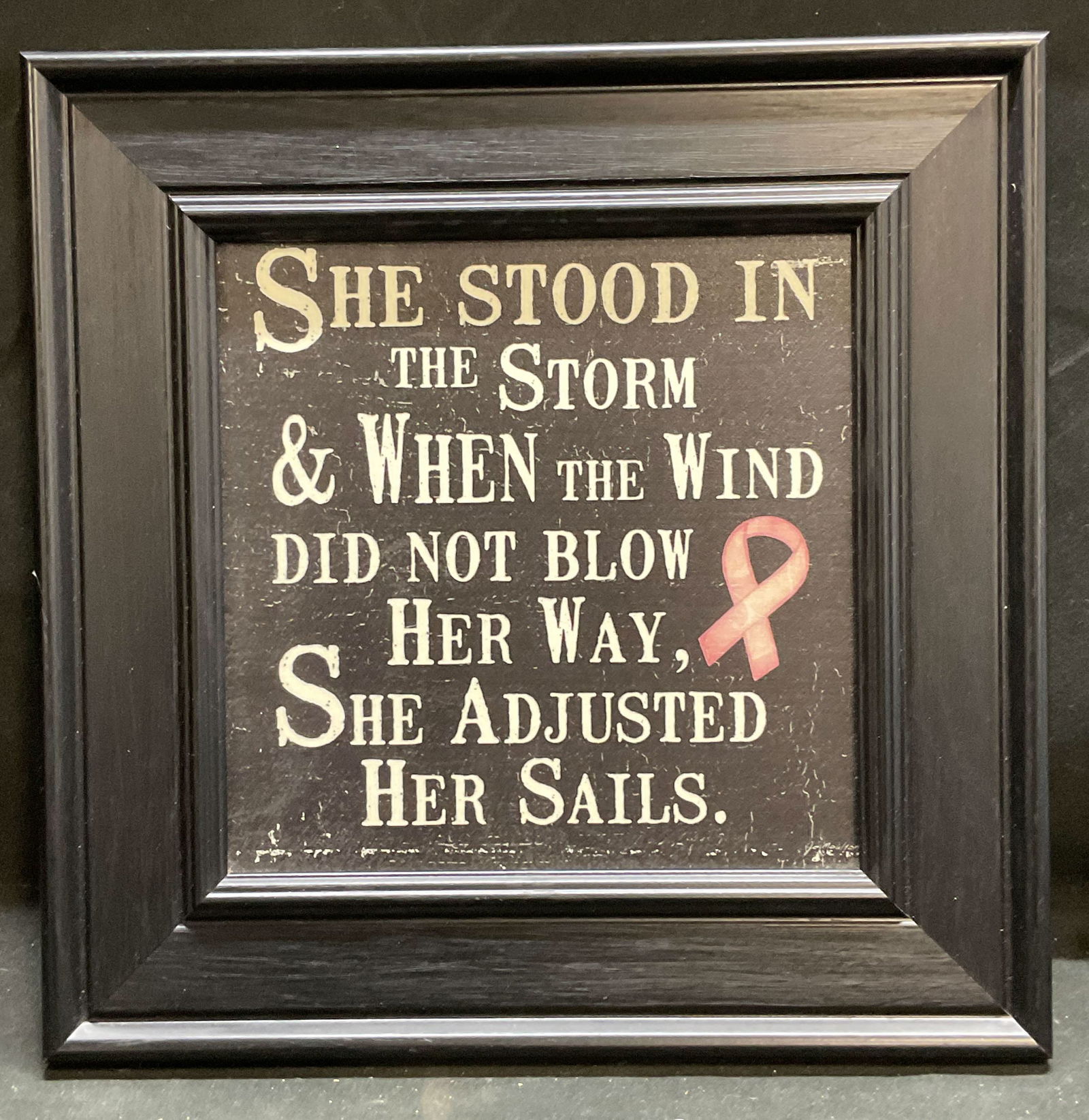 Framed Inspirational Quote Lithograph: Framed lithograph on board. Inspirational quote with pink ribbon. Reads She Stood In The Storm And When The Wind Did Not Blow Her Way She Adjusted Her Sails. Signed in print lower right, illegible. Bl