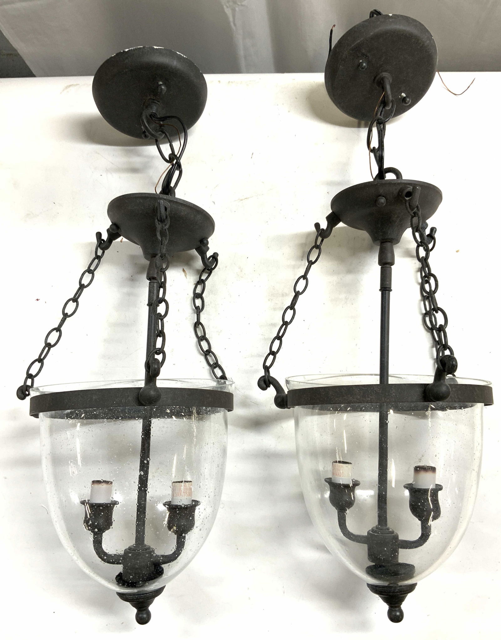 Pair Metal & Glass Bell Jar Lanterns: Lot includes 2 bell jar lanterns. Each arm glass and metal. Lanterns each have 2 arms. Bases are connected to tops by chain links. Each measure approx 23 inches tall 9 inches wide. Lanterns, lighting,