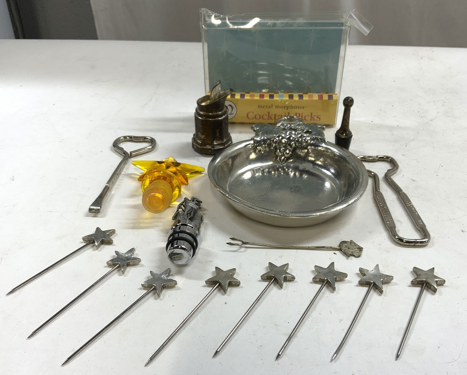 Lot 16 Assorted Tabletop Accessories: Lot includes 1 box of 8 metal star form Cocktail Picks, 1 pewter dish with grape and leaf handle trademarked WILLIAMS SONOMA MADE IN ITALY, 1 Farmhouse form hors doeuvres fork, 1 metal golf bag and cl