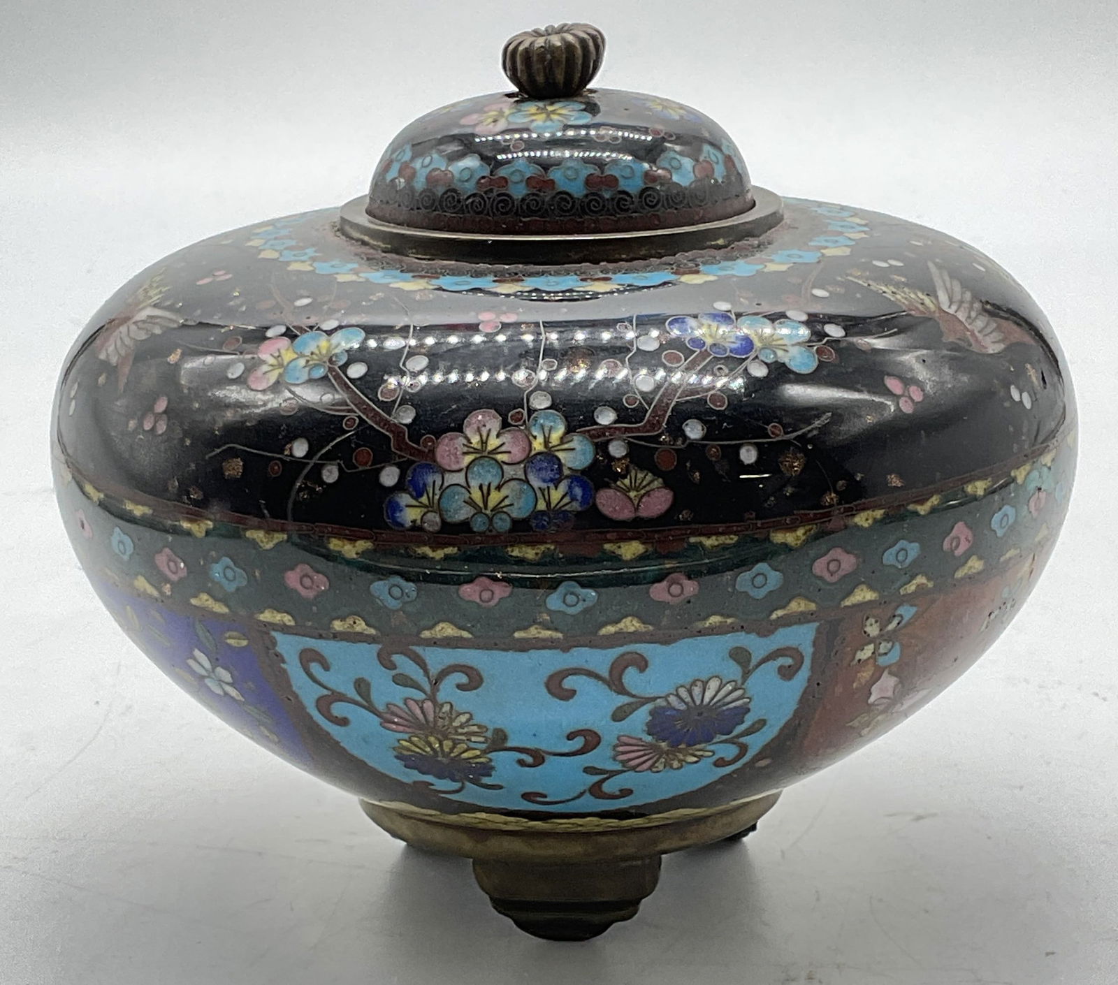 Vintage Asian Cloisonne Floral Lidded Jar: Vintage Asian cloisonne lidded jar. Enamel over brass, hand painted. Footed base. Cartouches and bands of floral and bird motifs. Palette of black, blue, pink, and red. Measures approx 5.5 x 4 inches.