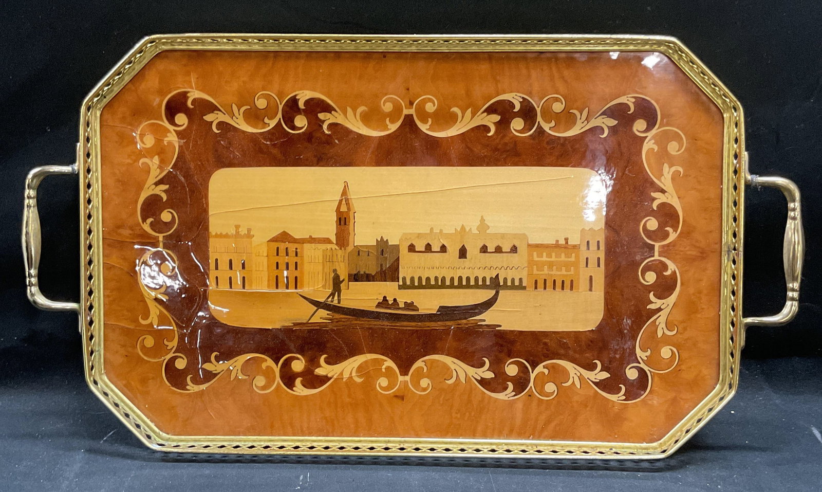 Venice Scene Marquetry Inlaid Wood Tray, Italy: Marquetry inlaid varnished wood tray with reticulated gold tone rim and handles. Venice scene with gondola and city motif. Made in Italy. Measures approx 16.5 x 9.25 inches. Wear including cracking to
