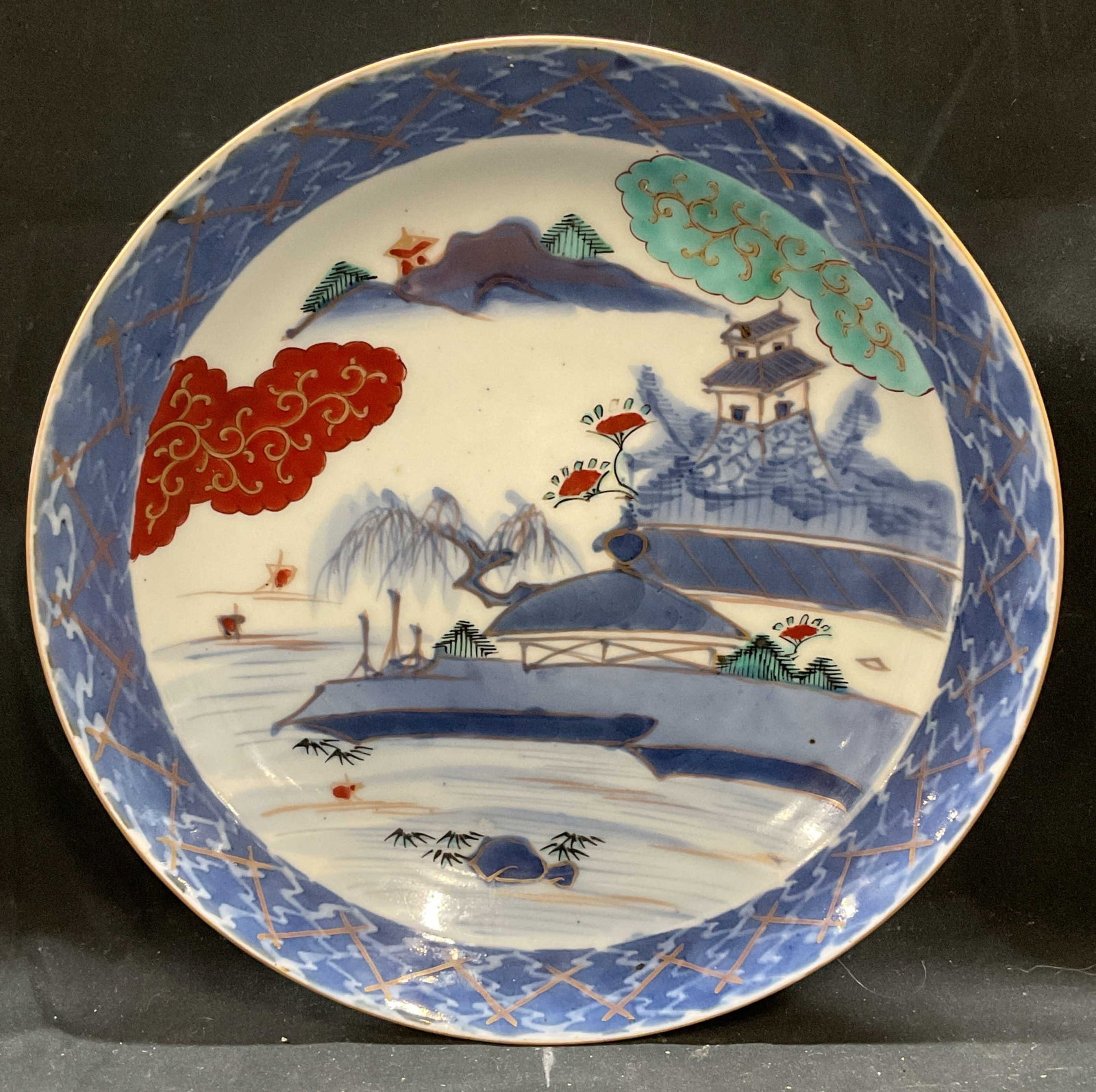 Vintage Japanese Porcelain Imari Plate: Vintage, possibly antique, Japanese porcelain Imari plate. Hand painted traditional landscape scene with gilt decoration. Palette of blue, red, and green. Measures approx 11.25 inches. Some wear inclu