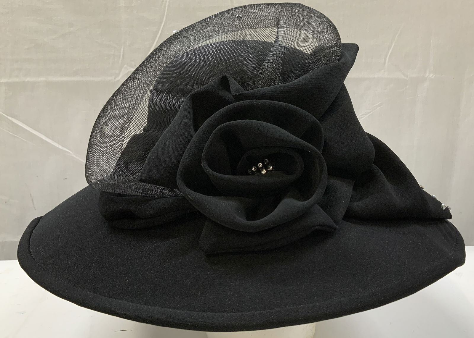 Perche COUTURE Black Formal Hat W Floral Accents: Elegant formal hat featuring a wide brim & a structured hard interior for a secure fit. Hat is decorated w a large flower & accented w small clusters of rhinestones. Features a layer of black mesh. Si