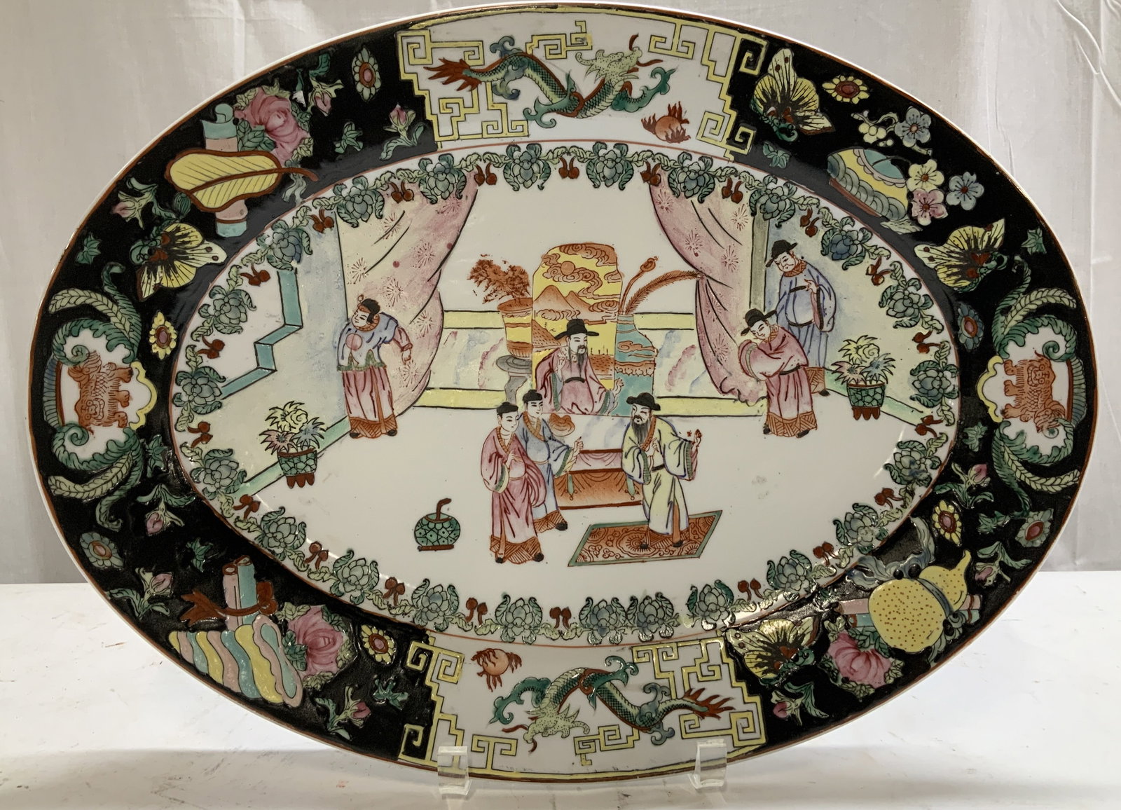 Vntg Chinese Famille Rose Painted Scenic Platter: Hand-painted porcelain platter featuring a hand-painted scene of Chinese figures in traditional attire. Figurines are surrounded by a floral & geometric border w pink, black, yellow & green tones. Top