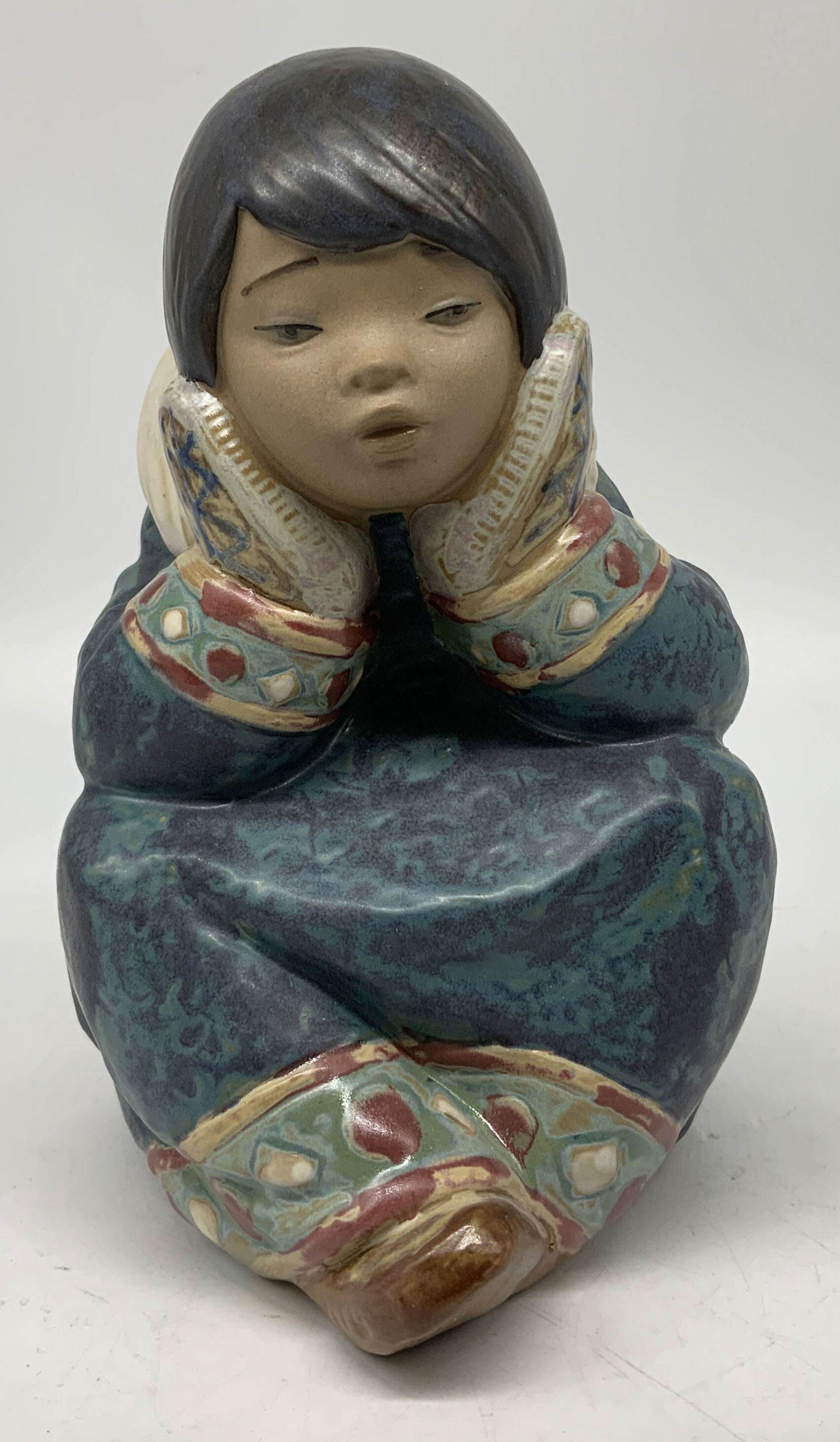 Lladro Pensive Eskimo Girl Ceramic Figurine SPAIN: Figurine depicts an Eskimo girl, with her hands resting on her cheeks. She is wearing a blue/green coat w patterned trim. Piece is ceramic. Signed & marked on underside. Reads, Lladro. HAND MADE IN SP