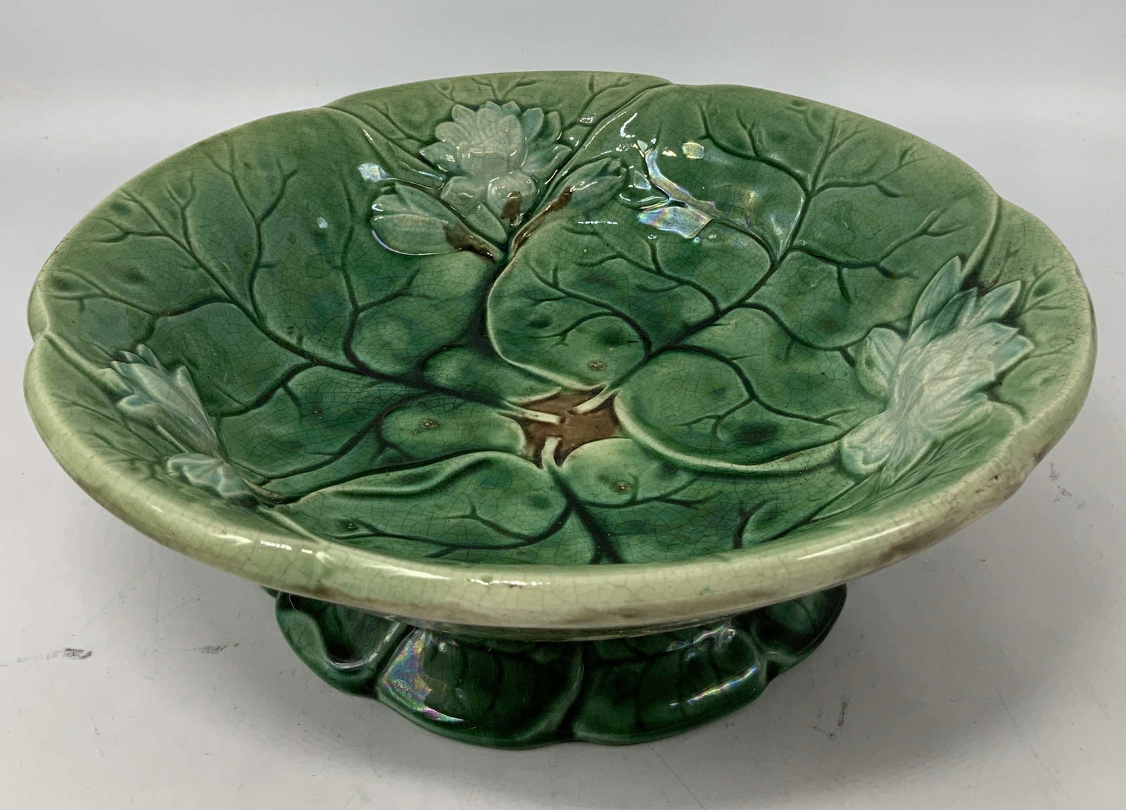 Vntg Majolica Green Lotus Leaf Pedestal Bowl: Vintage majolica style pedestal bowl featuring a detailed lotus leaf in a green glaze. Glossy finish. Surface wear consistent to age, use & exposure. Measurements: length 9.6in x width 9.6in x height