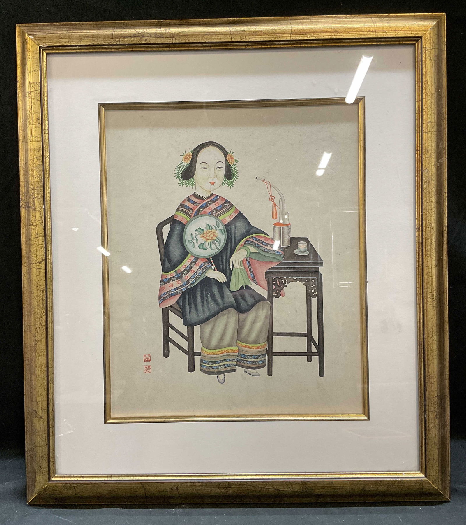 Framed Chinese Seated Woman Painting: Framed and matted painting on paper. Traditional Chinese scene, seated woman holding fan and pipe. Red seal at lower left. Gilt wood frame. Not examined out of frame. Frame measures approx 18 x 15.75